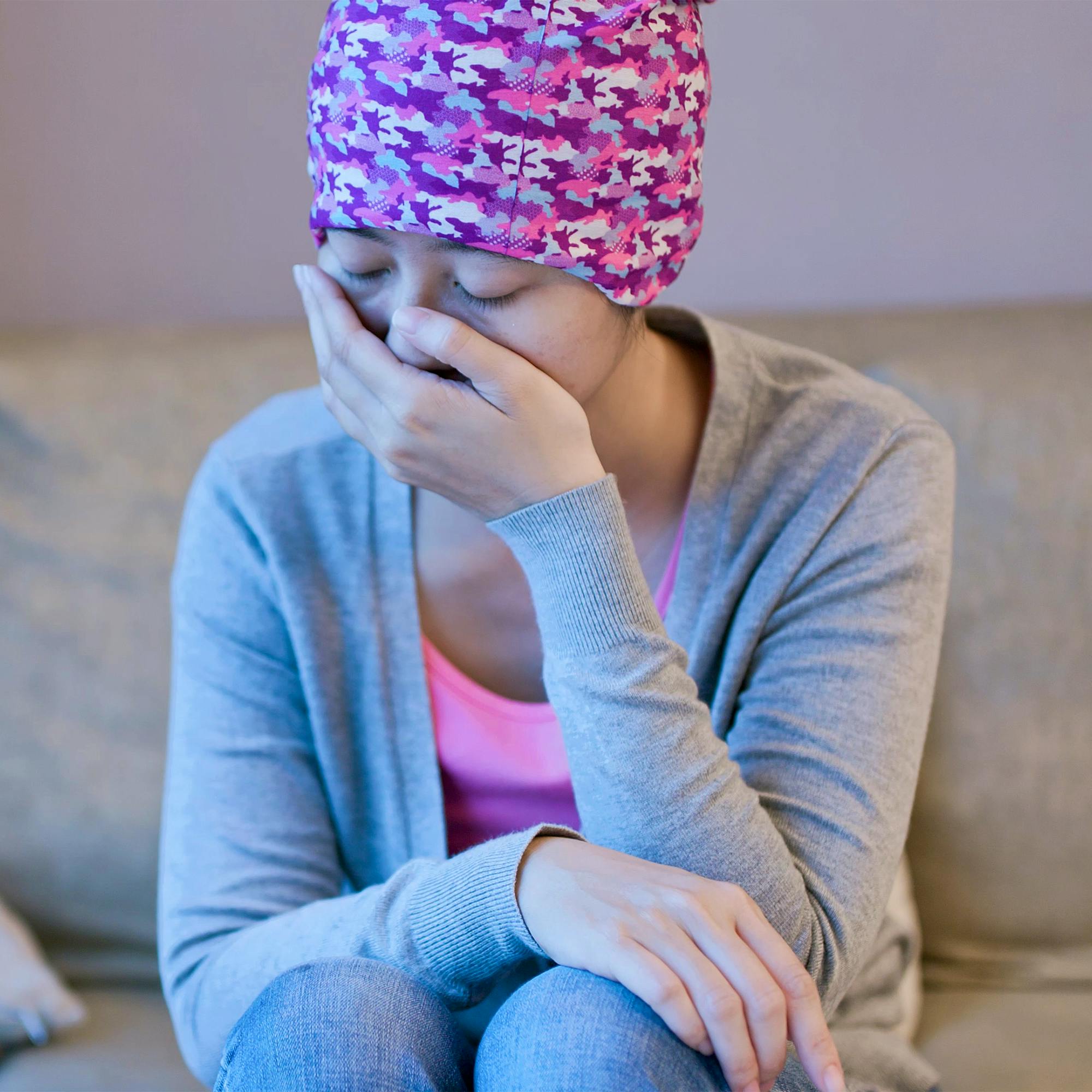 A woman with cancer is sitting on her couch, tired and in pain.