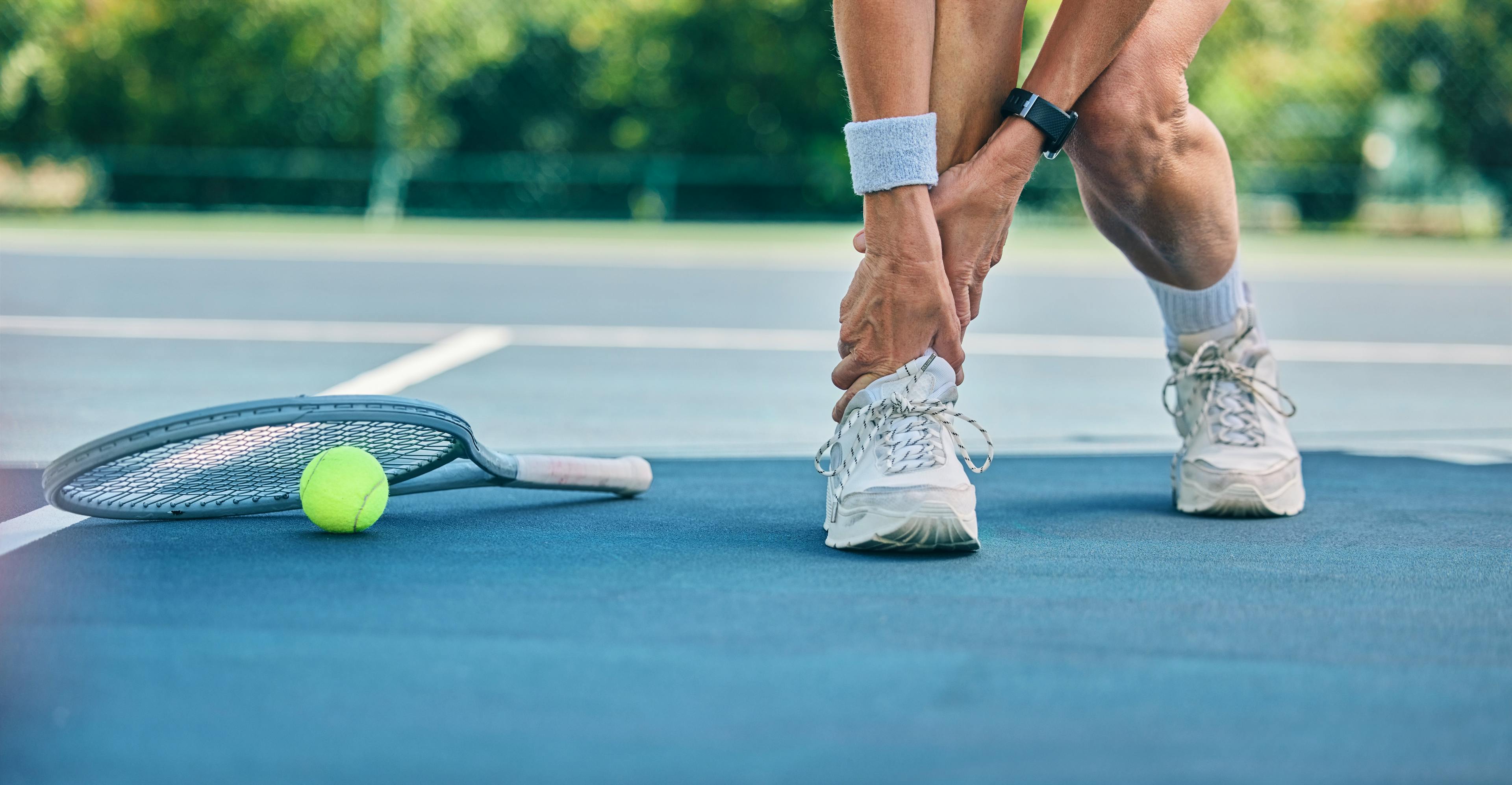 Person holding their ankle on tennis court after injury
