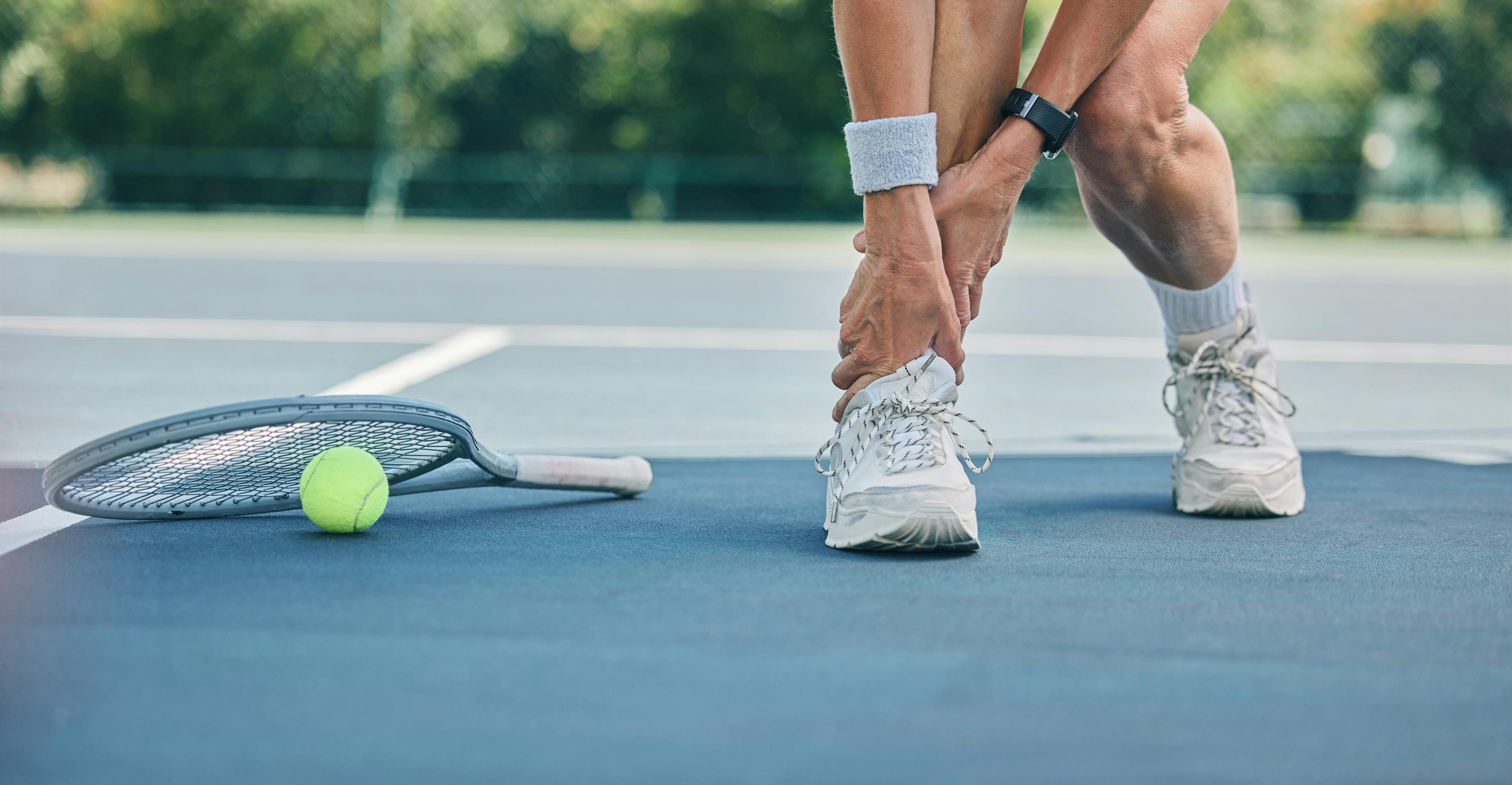 Person holding their ankle on tennis court after injury