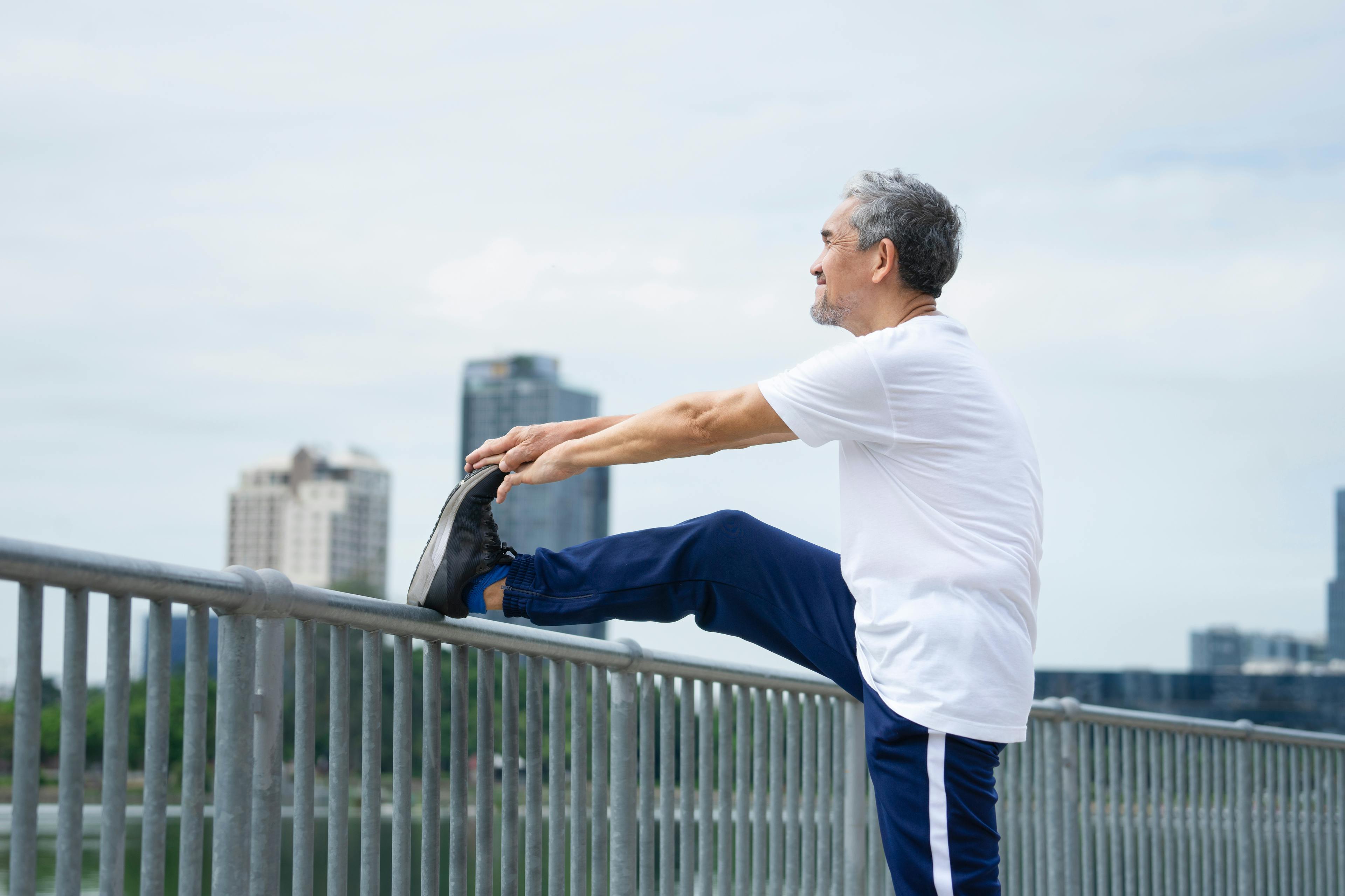 Older adult stretching their leg on a railing outdoors to improve knee mobility after joint injections