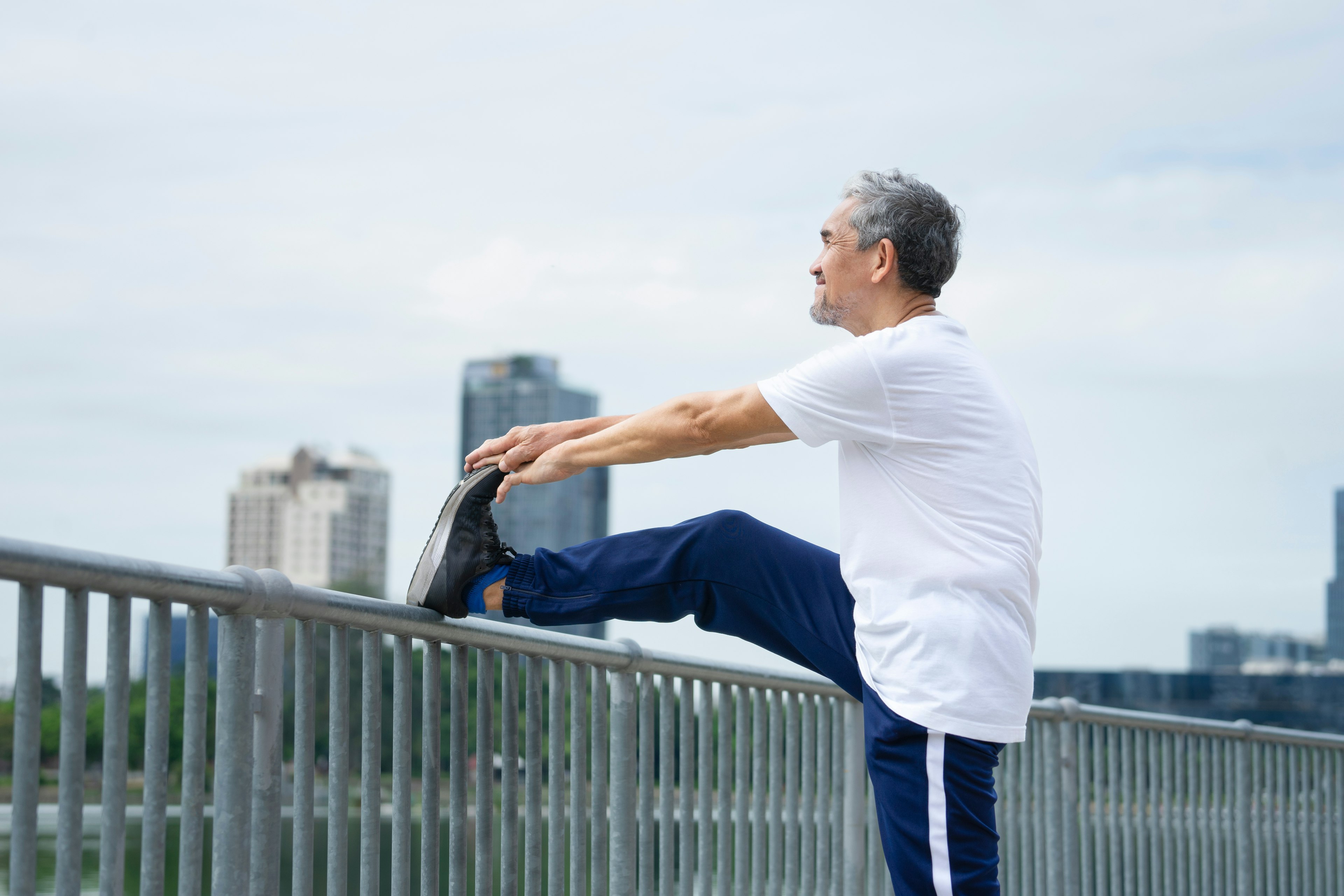 Older adult stretching their leg on a railing outdoors to improve knee mobility after joint injections