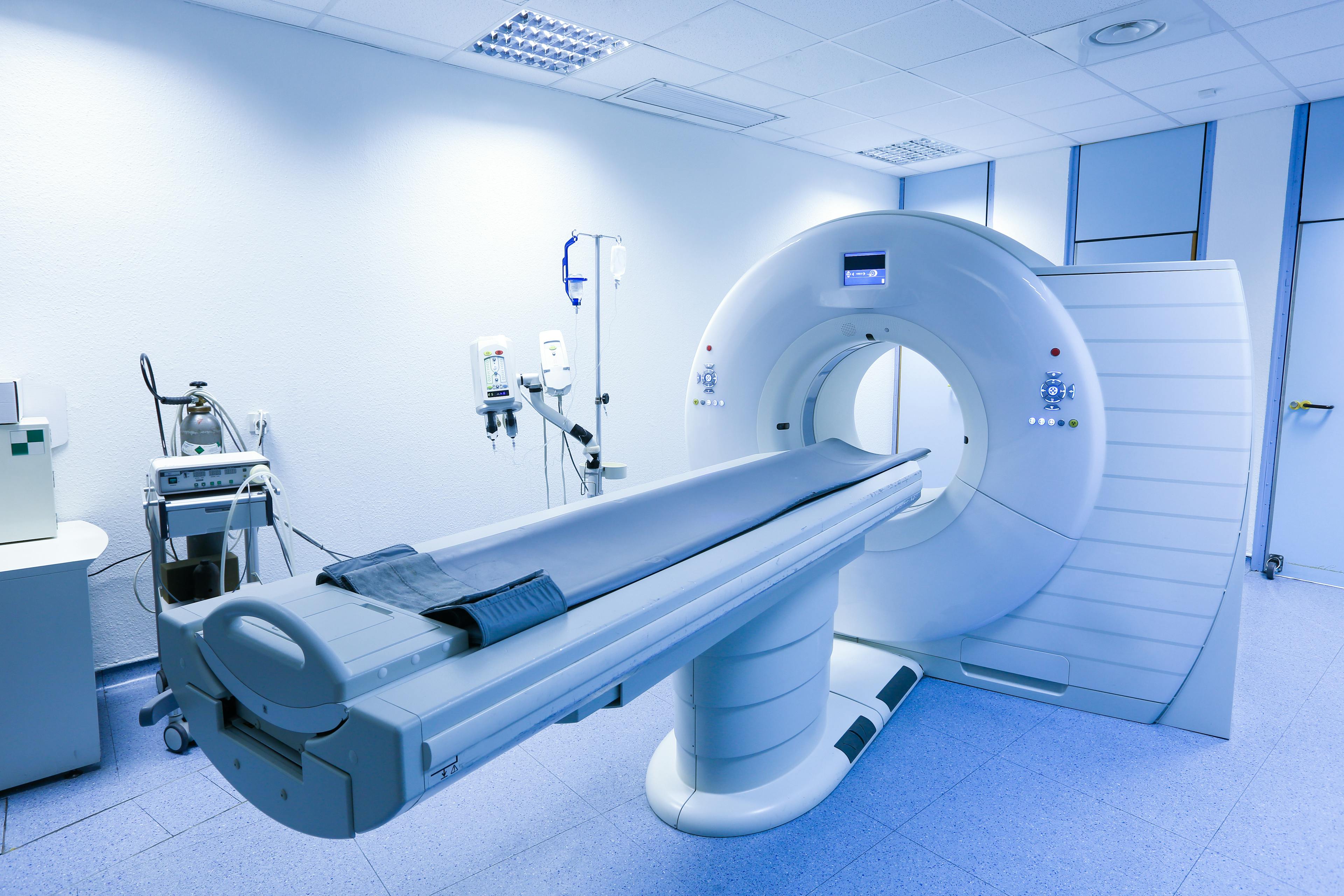 Empty medical imaging room with a CT scanner and patient table.