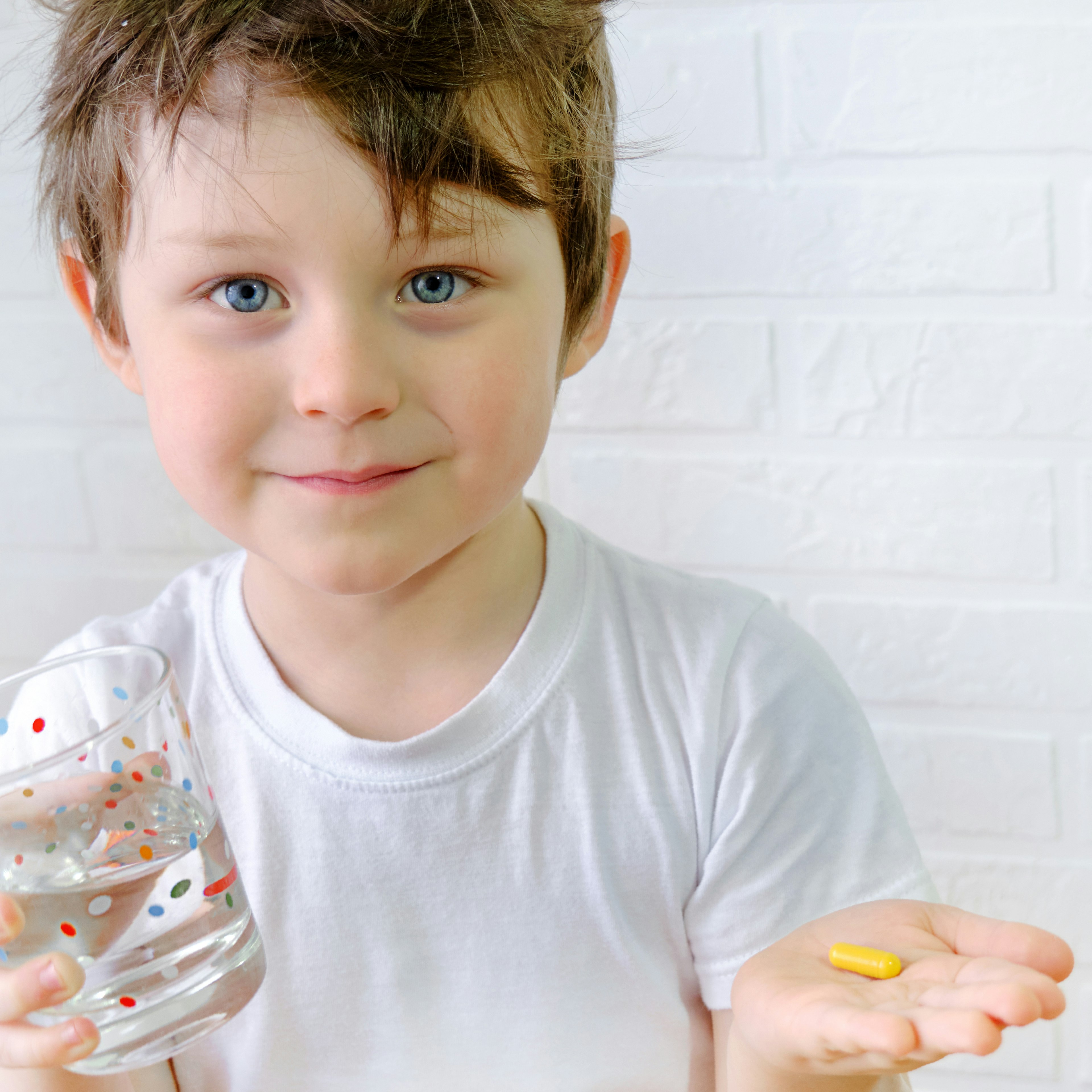 A child smiling holding a glass of water and his pill medication. 