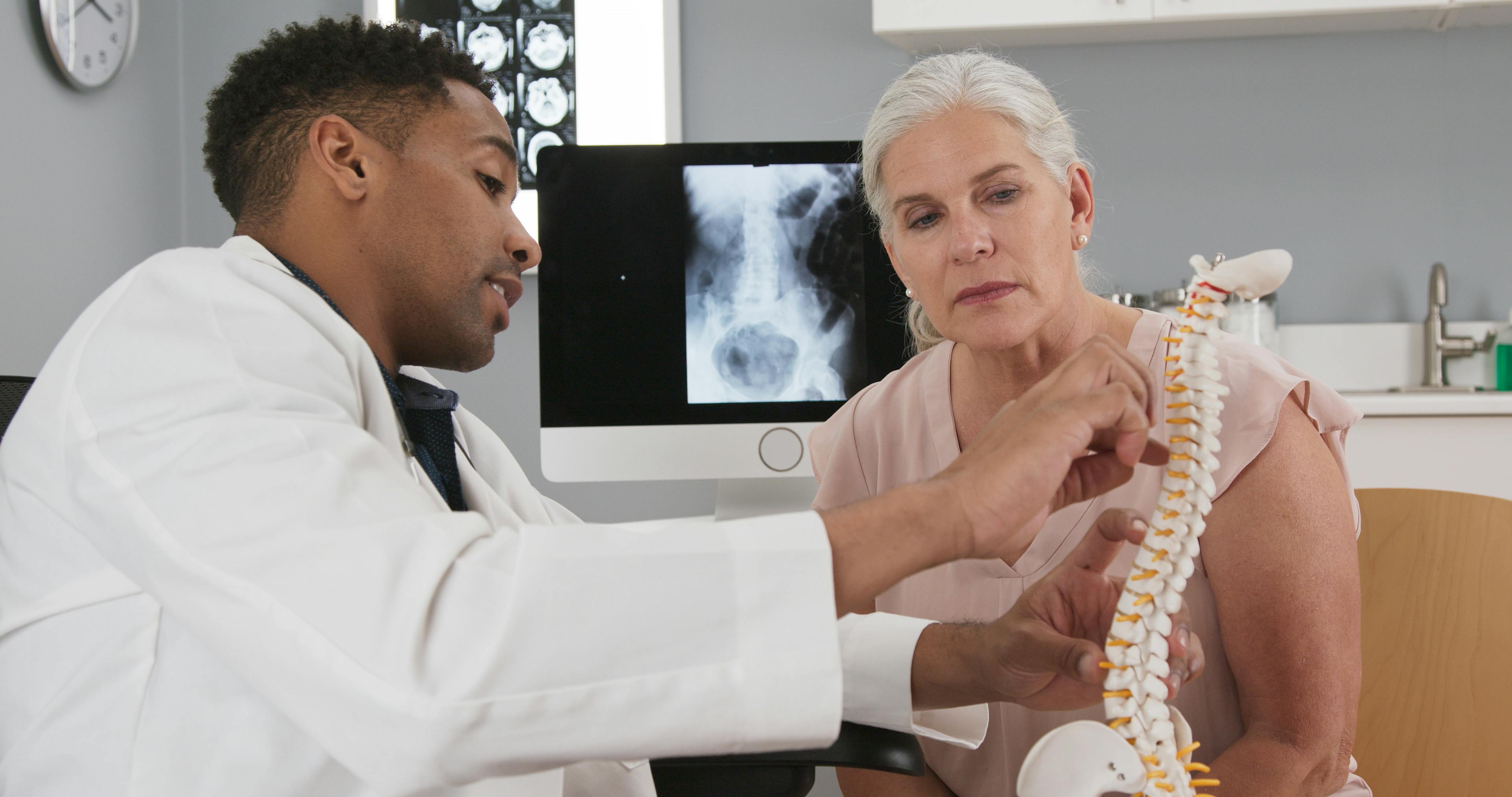 Pain management specialist explaining a spine model to a patient during a consultation in a medical office.