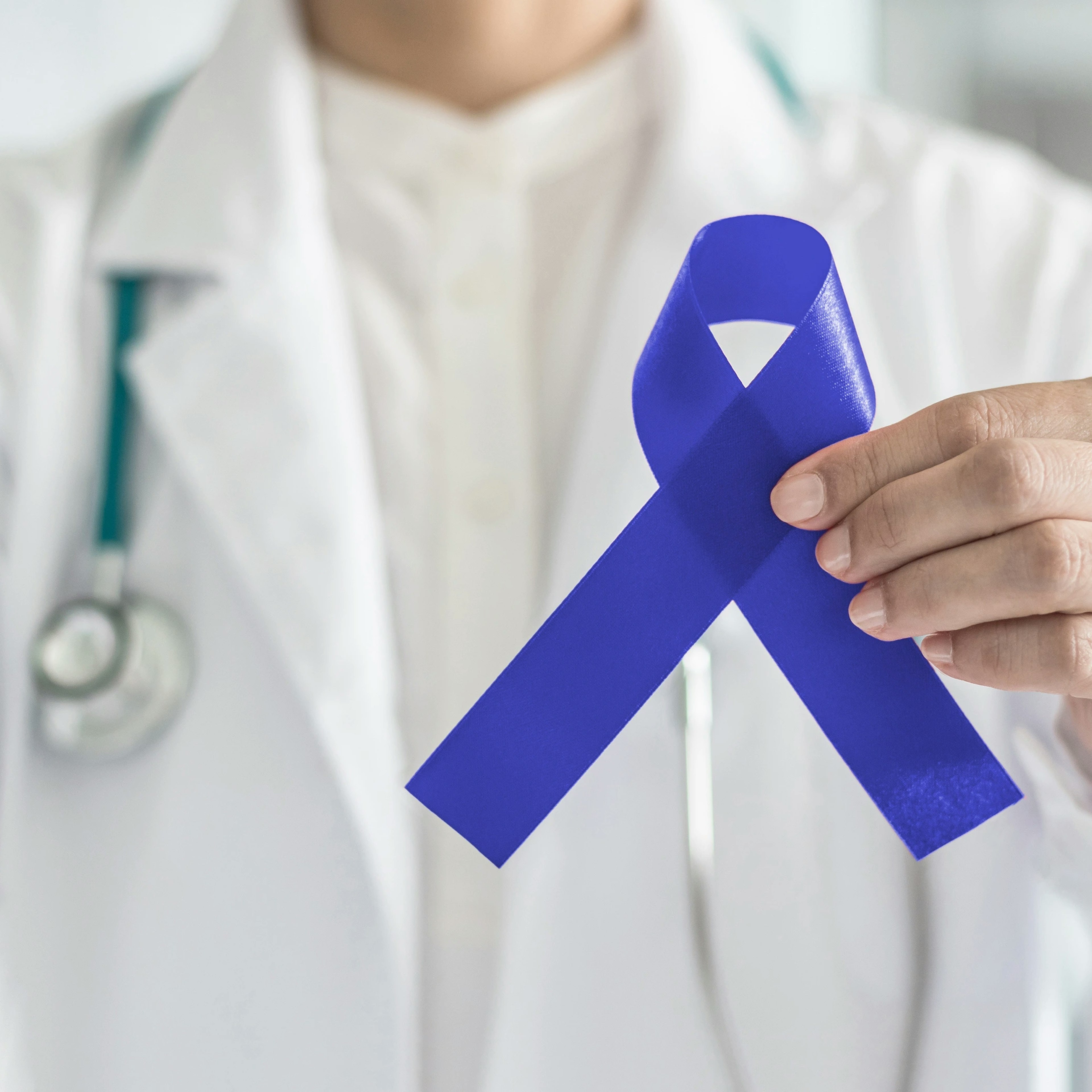 A medical provider is holding up a dark blue ribbon in support of colorectal cancer awareness month.