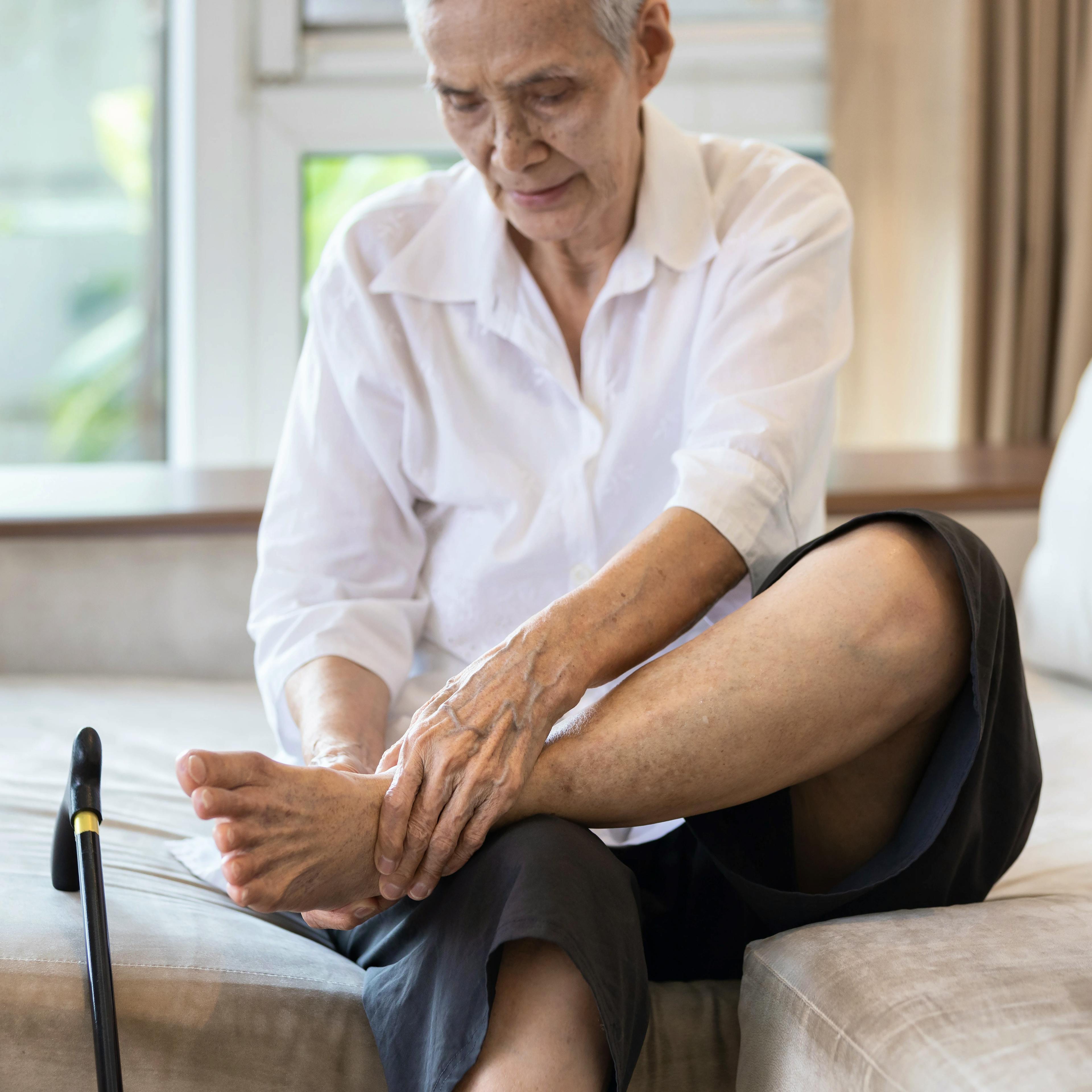An elderly person is grabbing their foot in pain due to peripheral neuropathy.