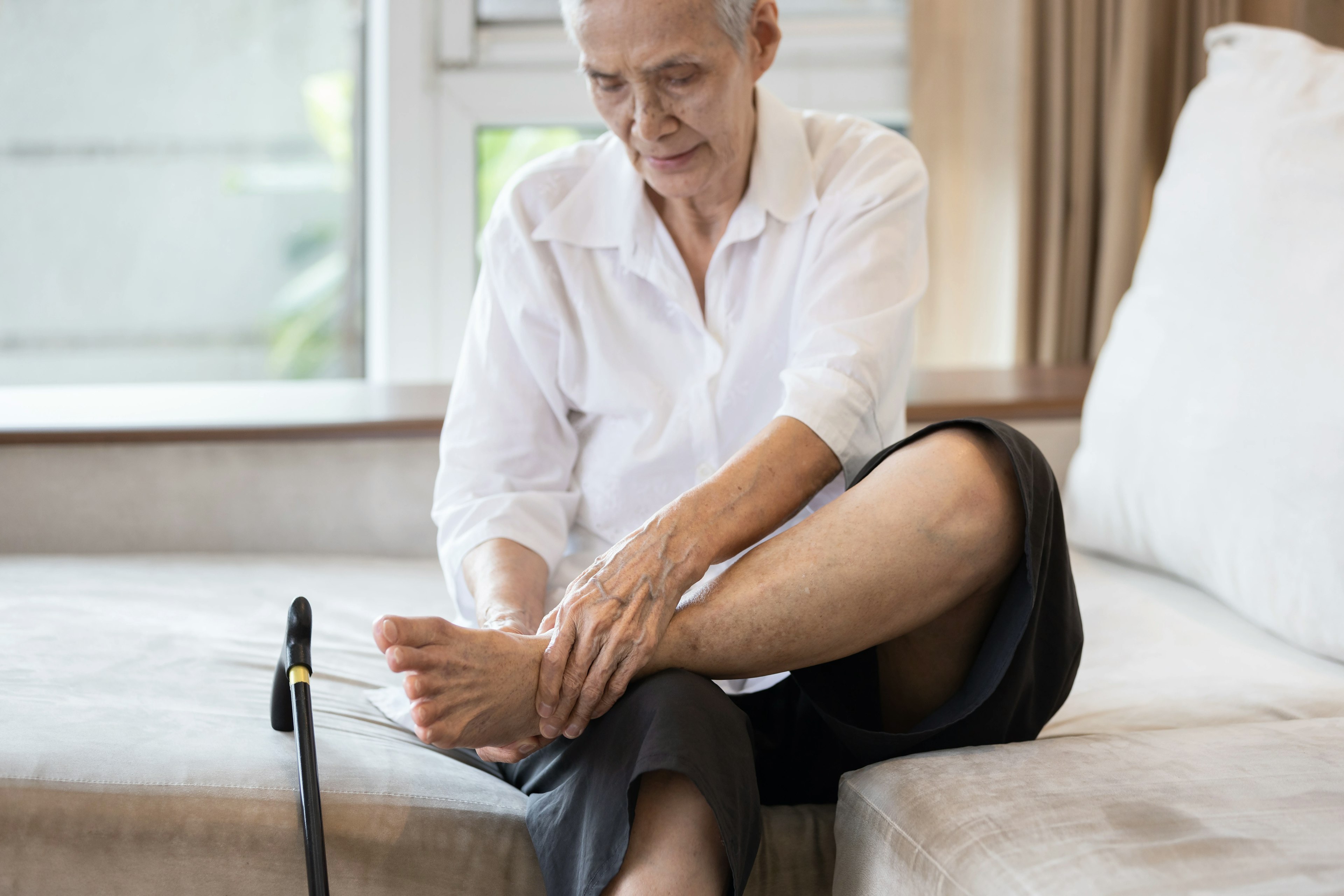 An elderly person is grabbing their foot in pain due to peripheral neuropathy.