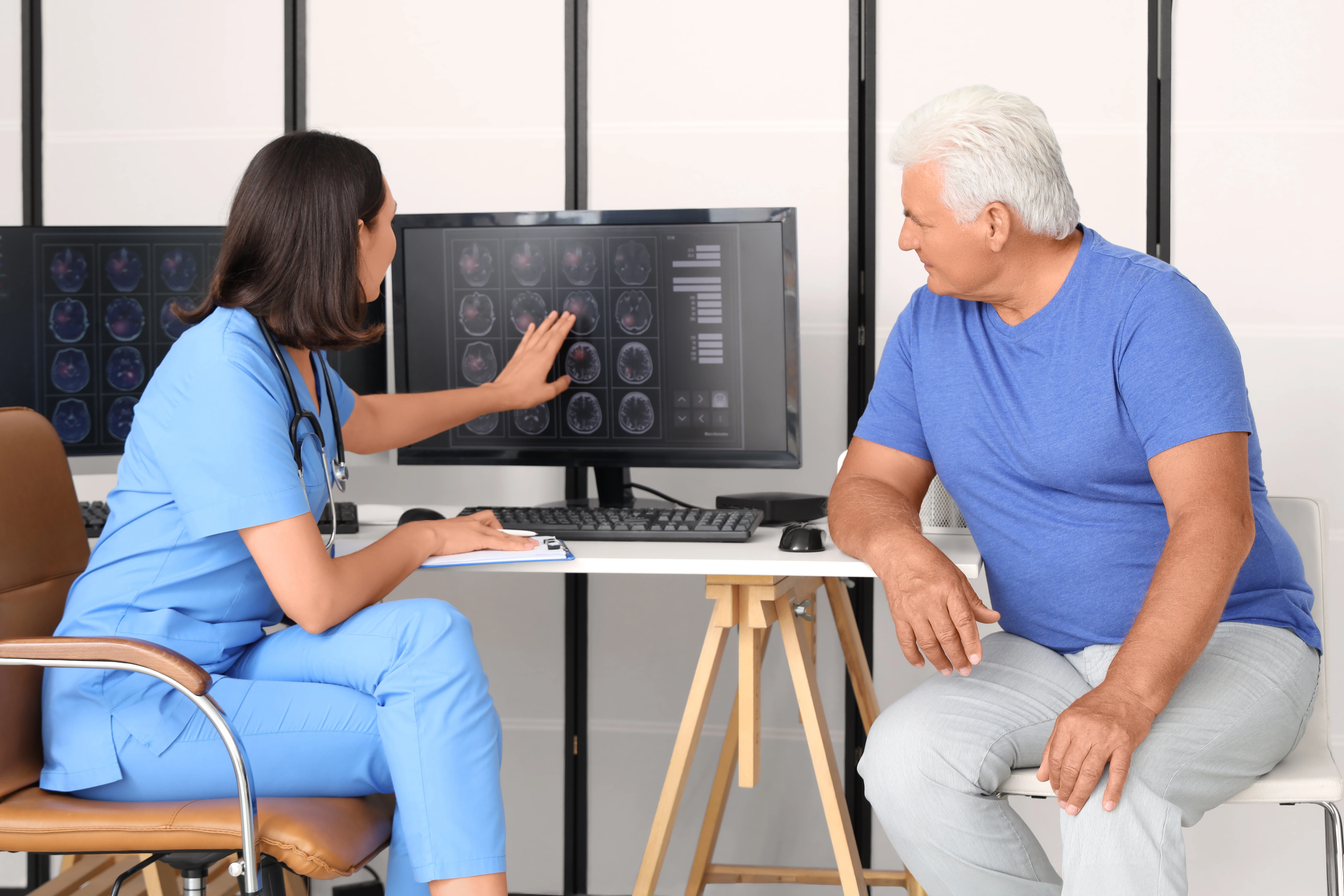 A female neurologist is walking her elderly male patient through the imaging scans of his brain.