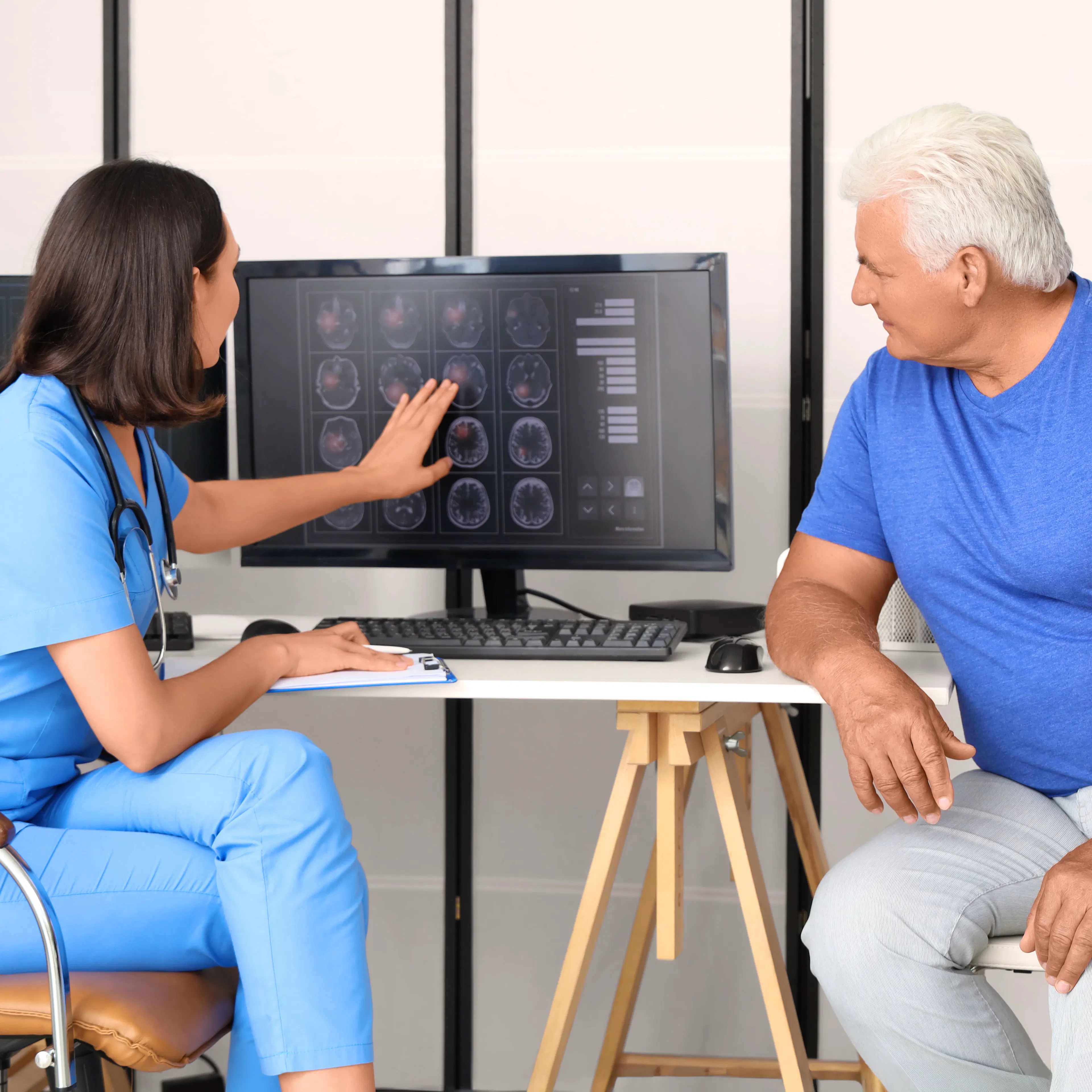 A female neurologist is walking her elderly male patient through the imaging scans of his brain.