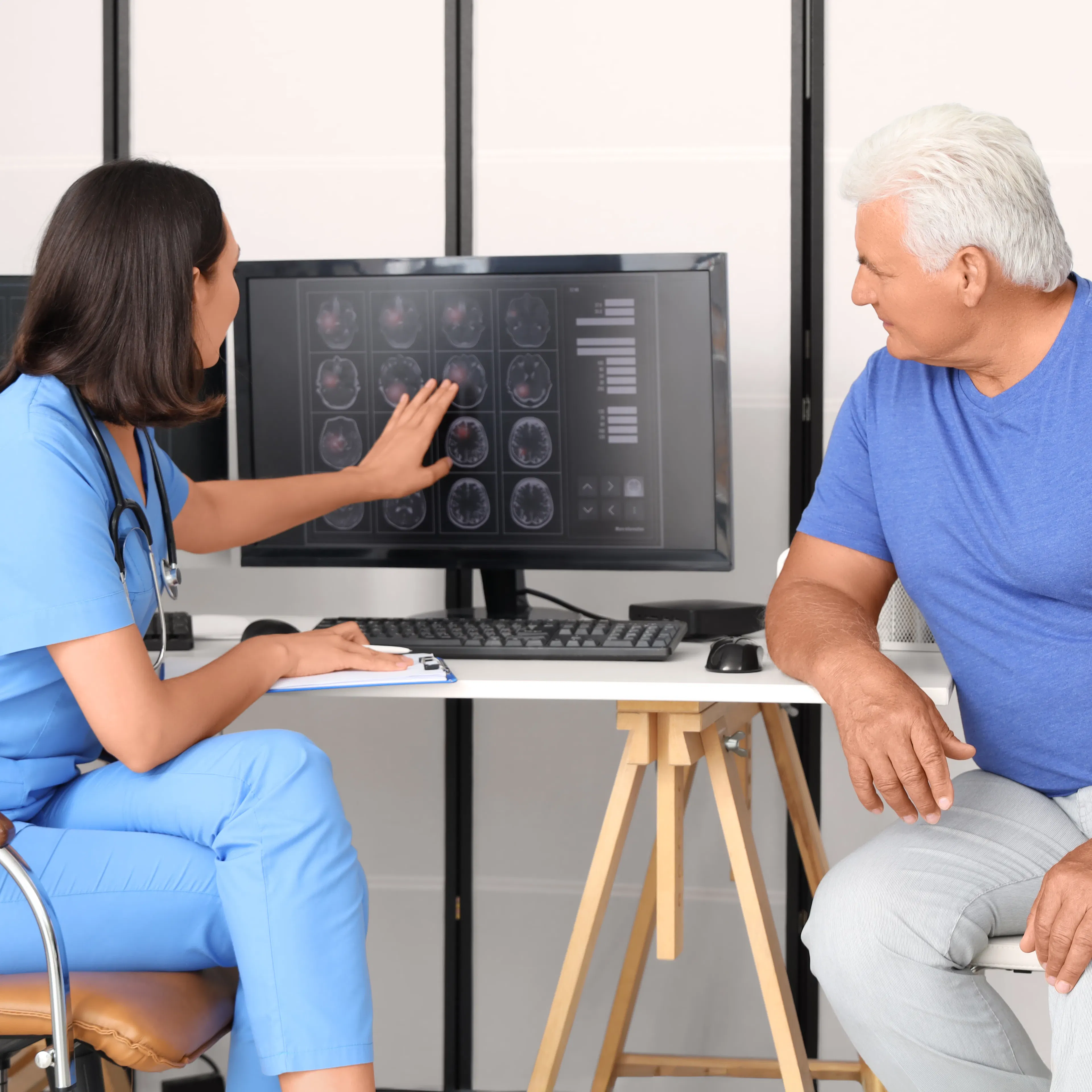 A female neurologist is walking her elderly male patient through the imaging scans of his brain.