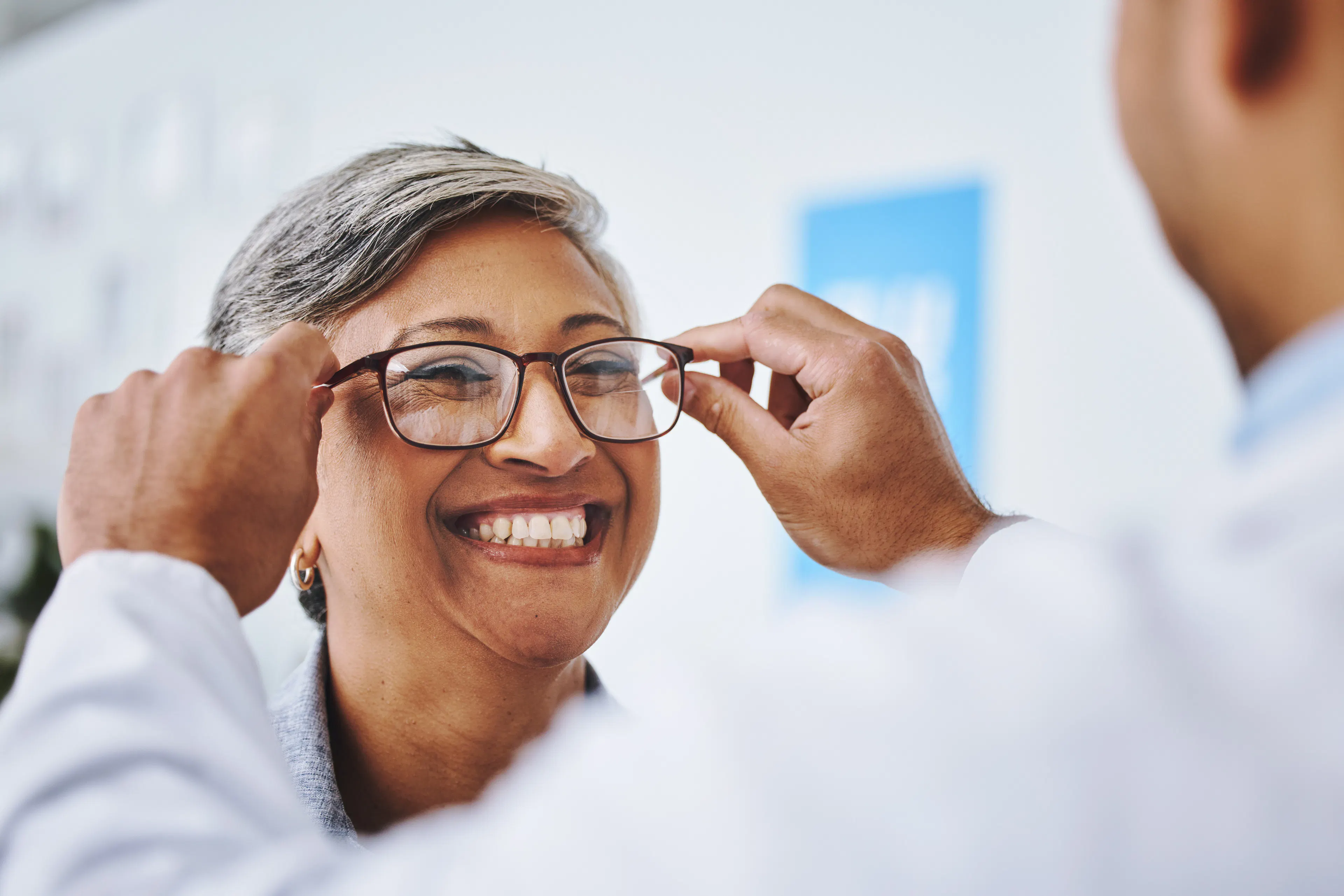 A female patient is at the eye doctor's clinic, happily trying on a pair of frames.