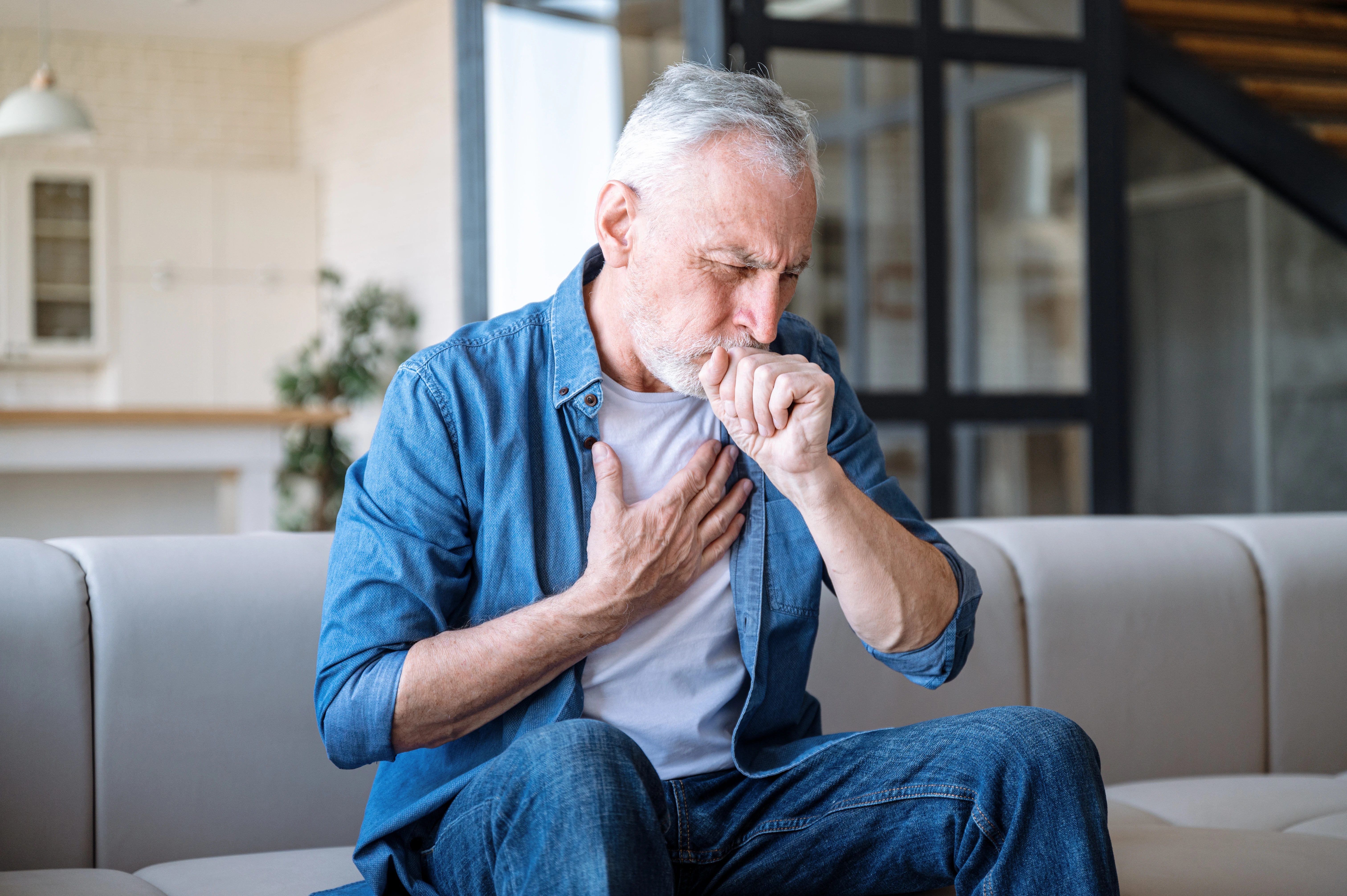 An elderly man is holding his chest and holding his fist to his mouth, indicating congestion or mucus build up.
