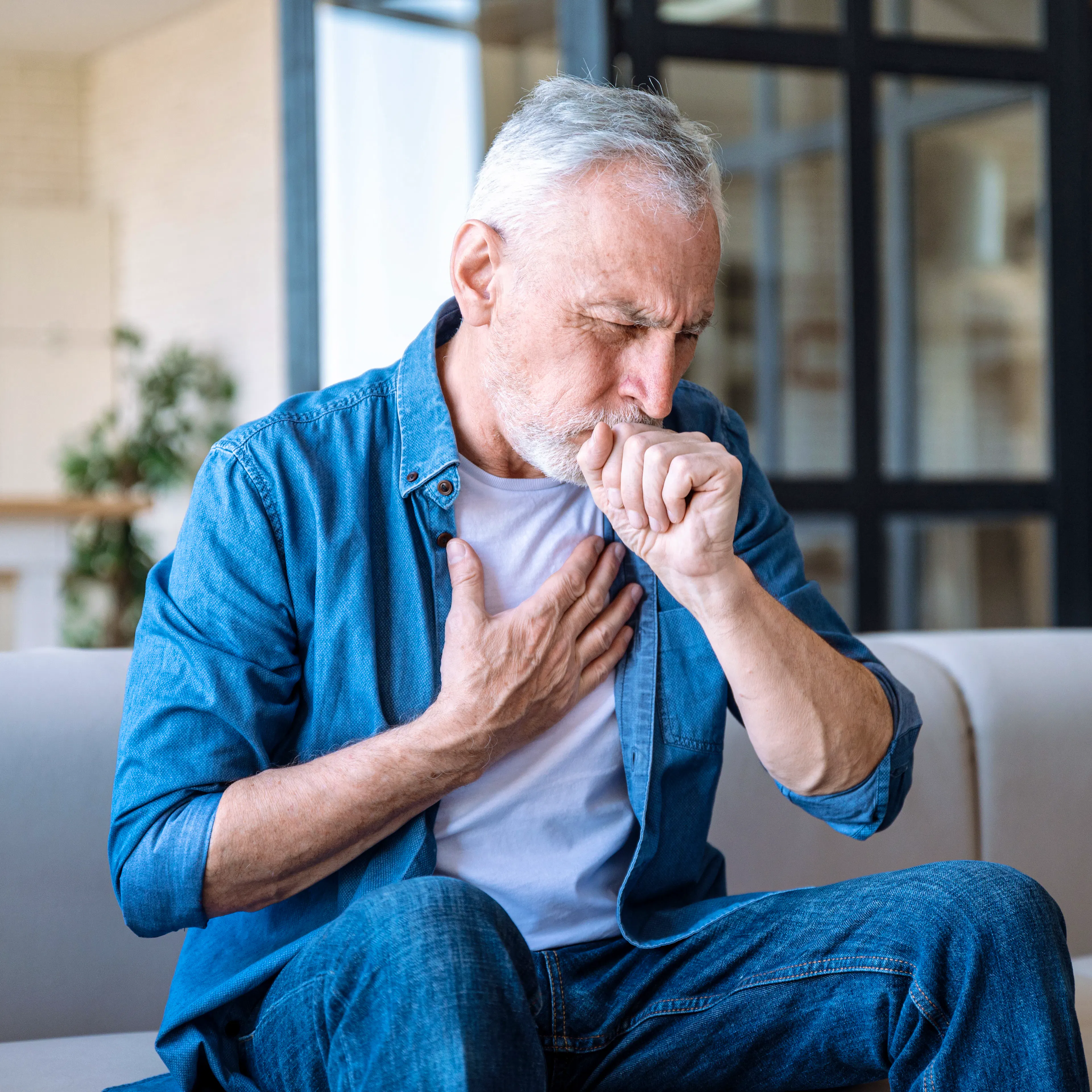 An elderly man is holding his chest and holding his fist to his mouth, indicating congestion or mucus build up.