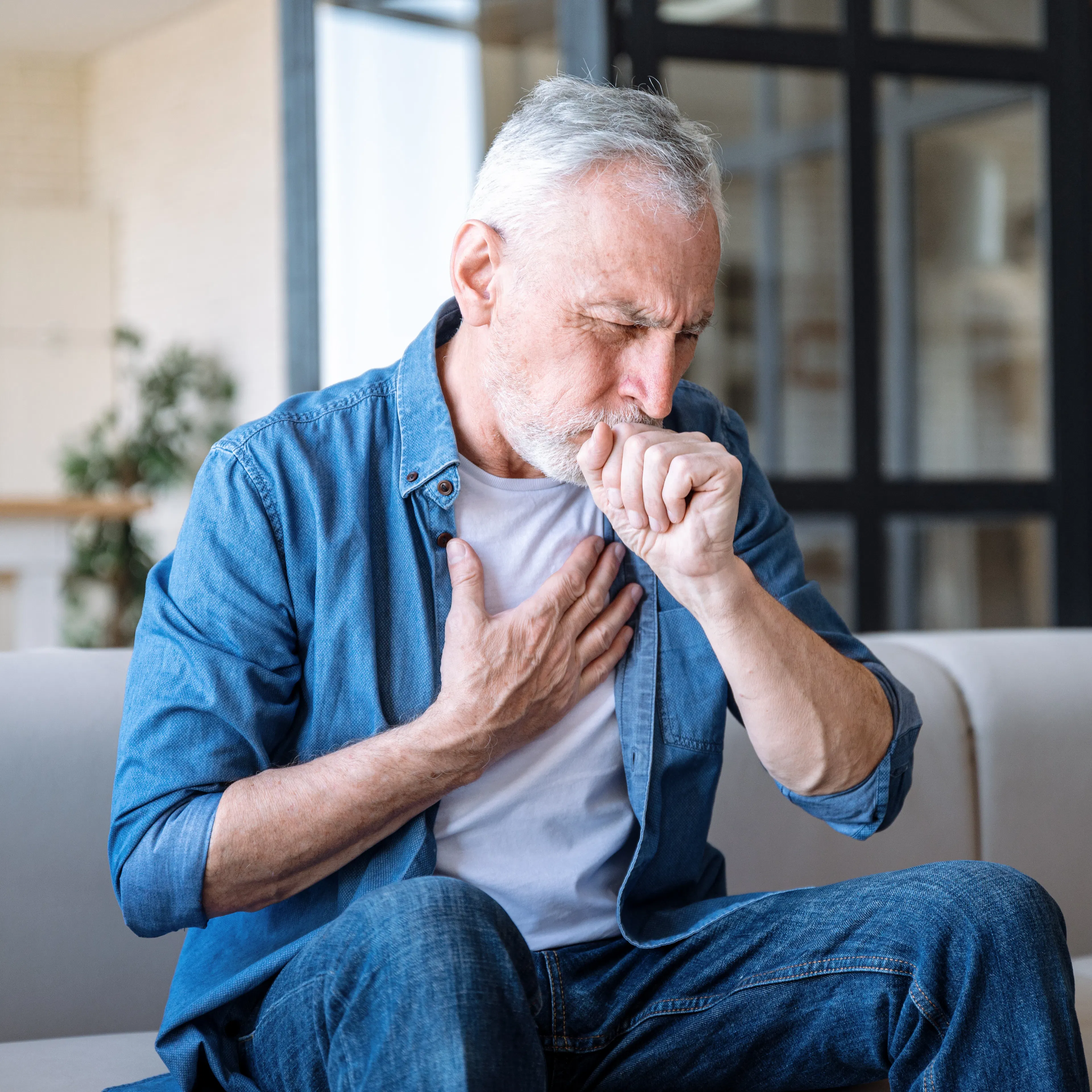 An elderly man is holding his chest and holding his fist to his mouth, indicating congestion or mucus build up.