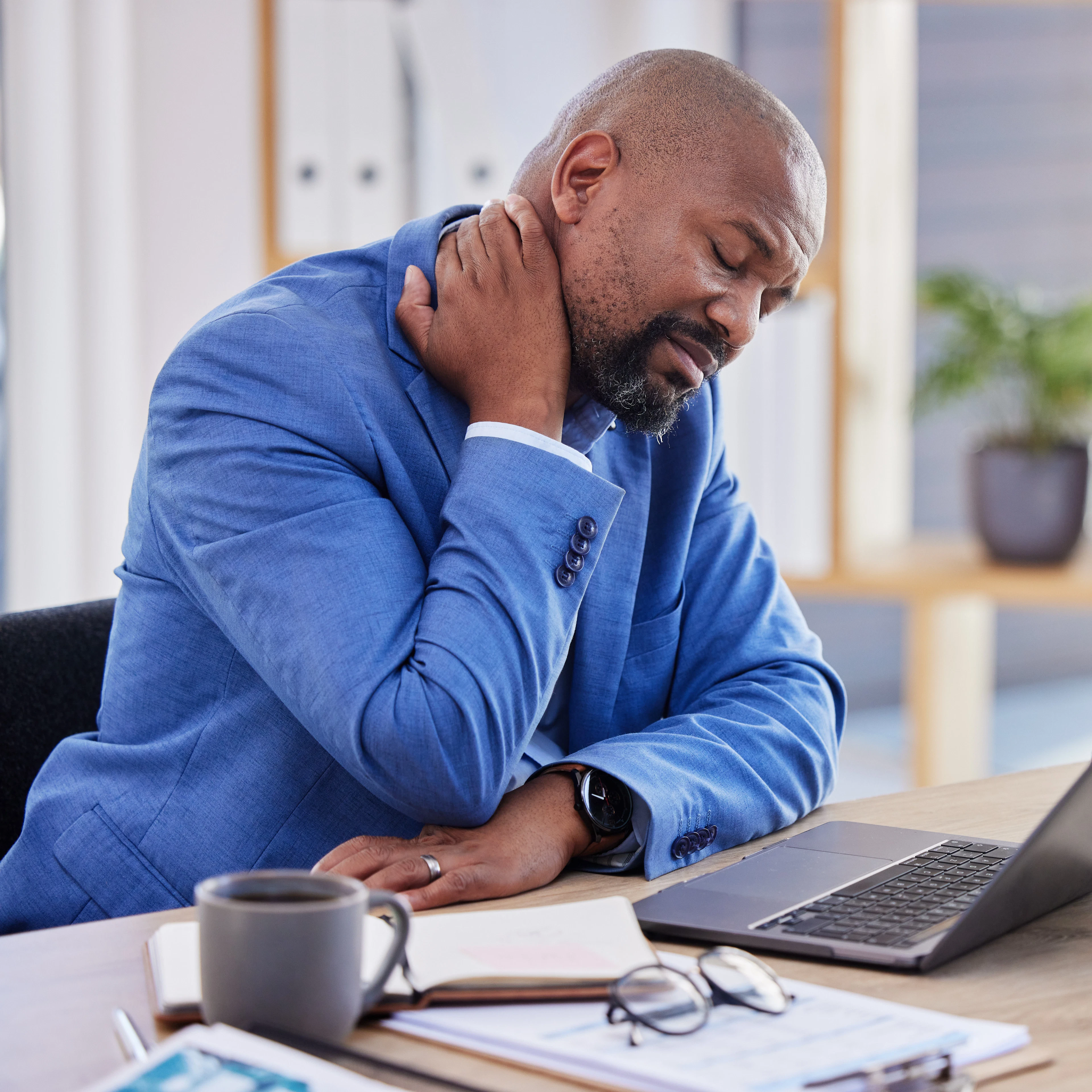 A male professional in a suit is holding his head in discomfort.