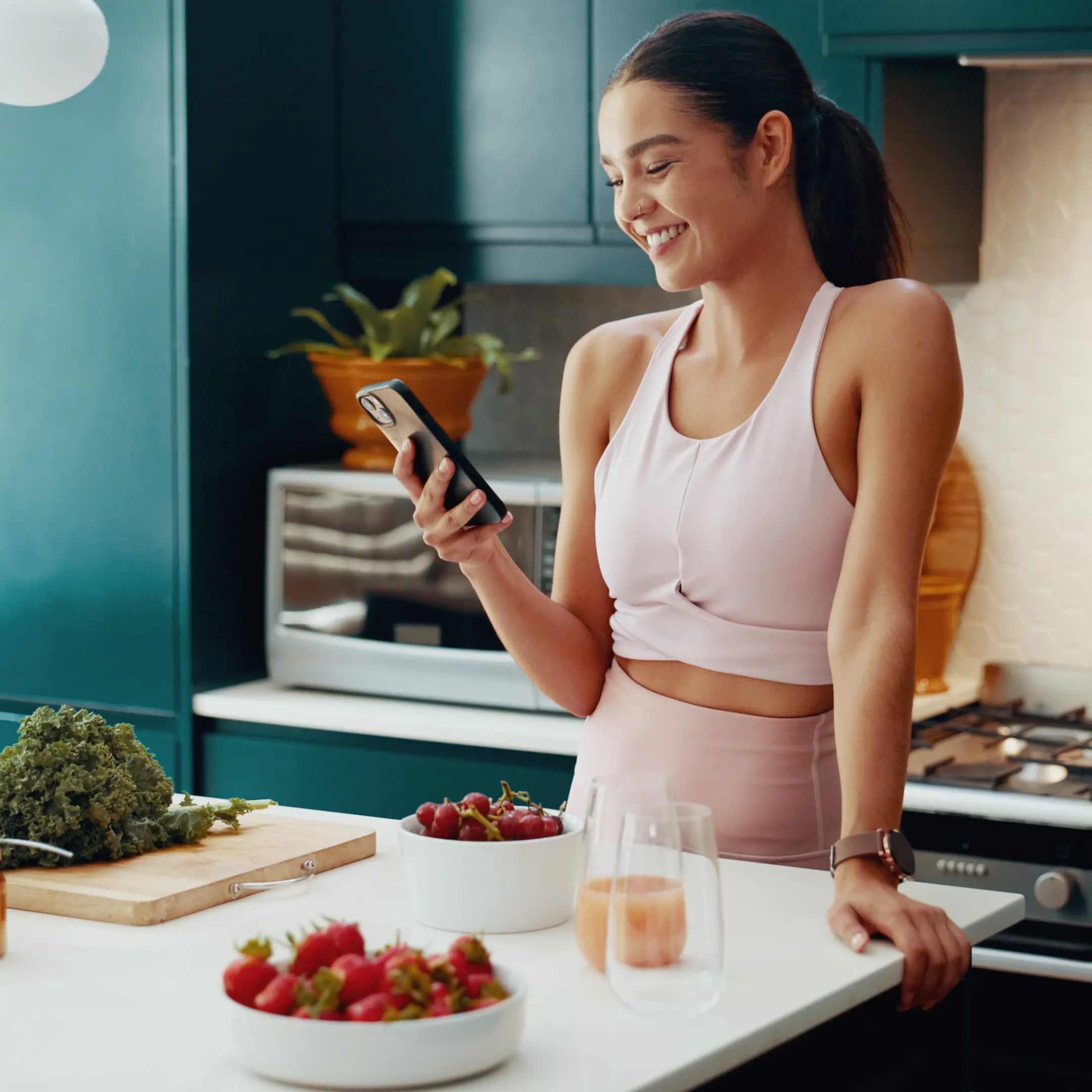 A fit woman is looking at her smartphone while preparing food, presumably to track her nutrition.