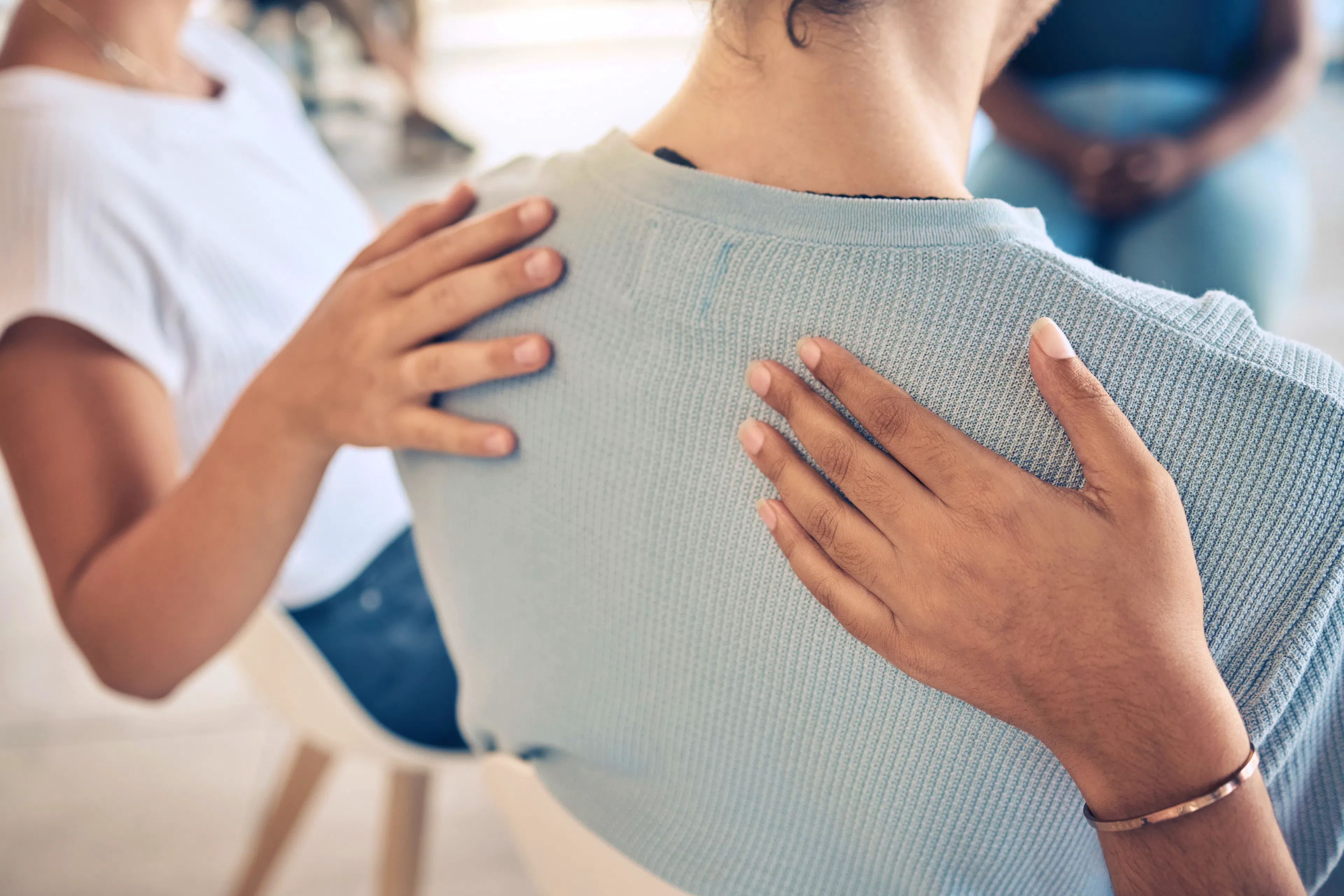 Two different people are placing their hands on someone's back to show support.