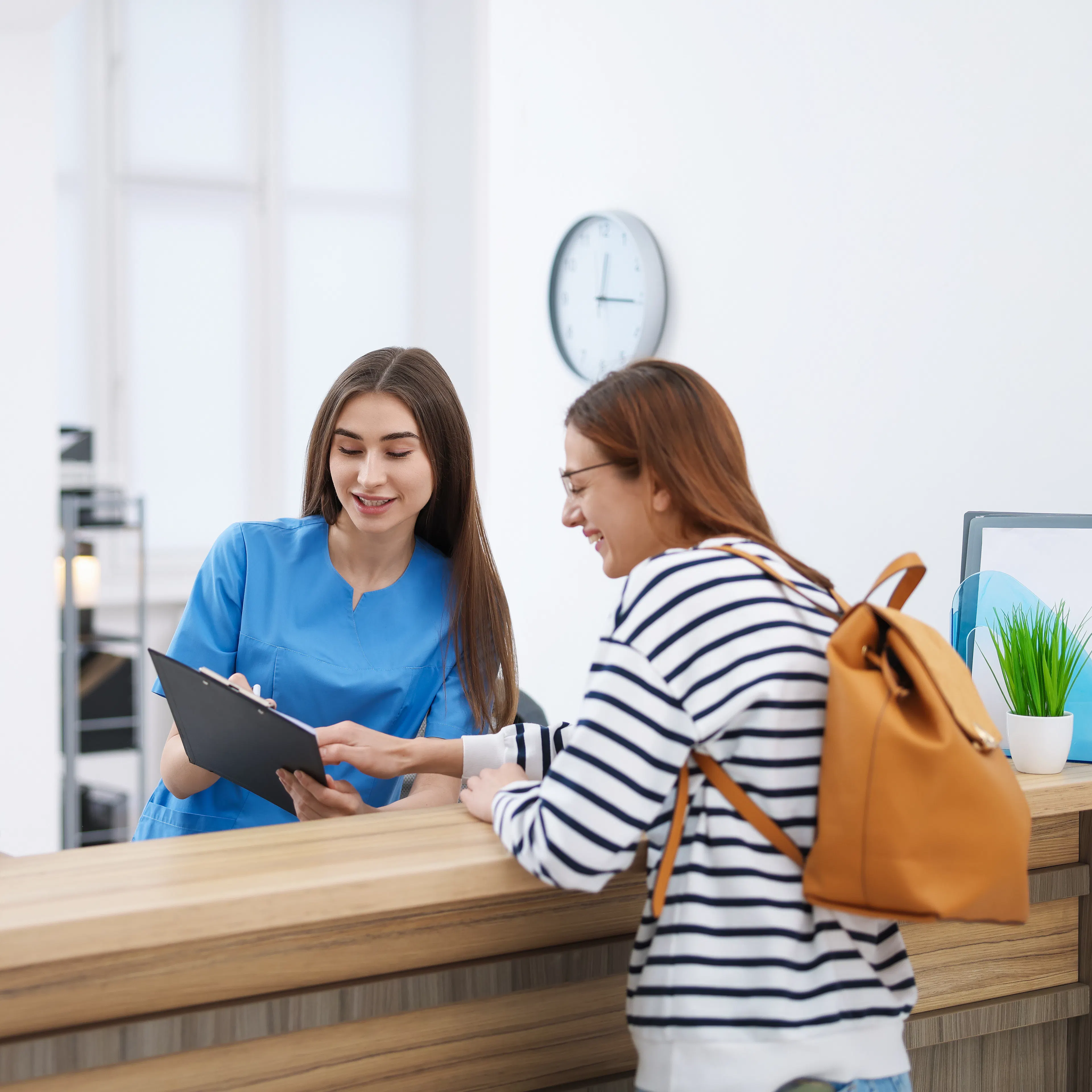 A front desk worker at a clinic is helping a patient, who looks happy.