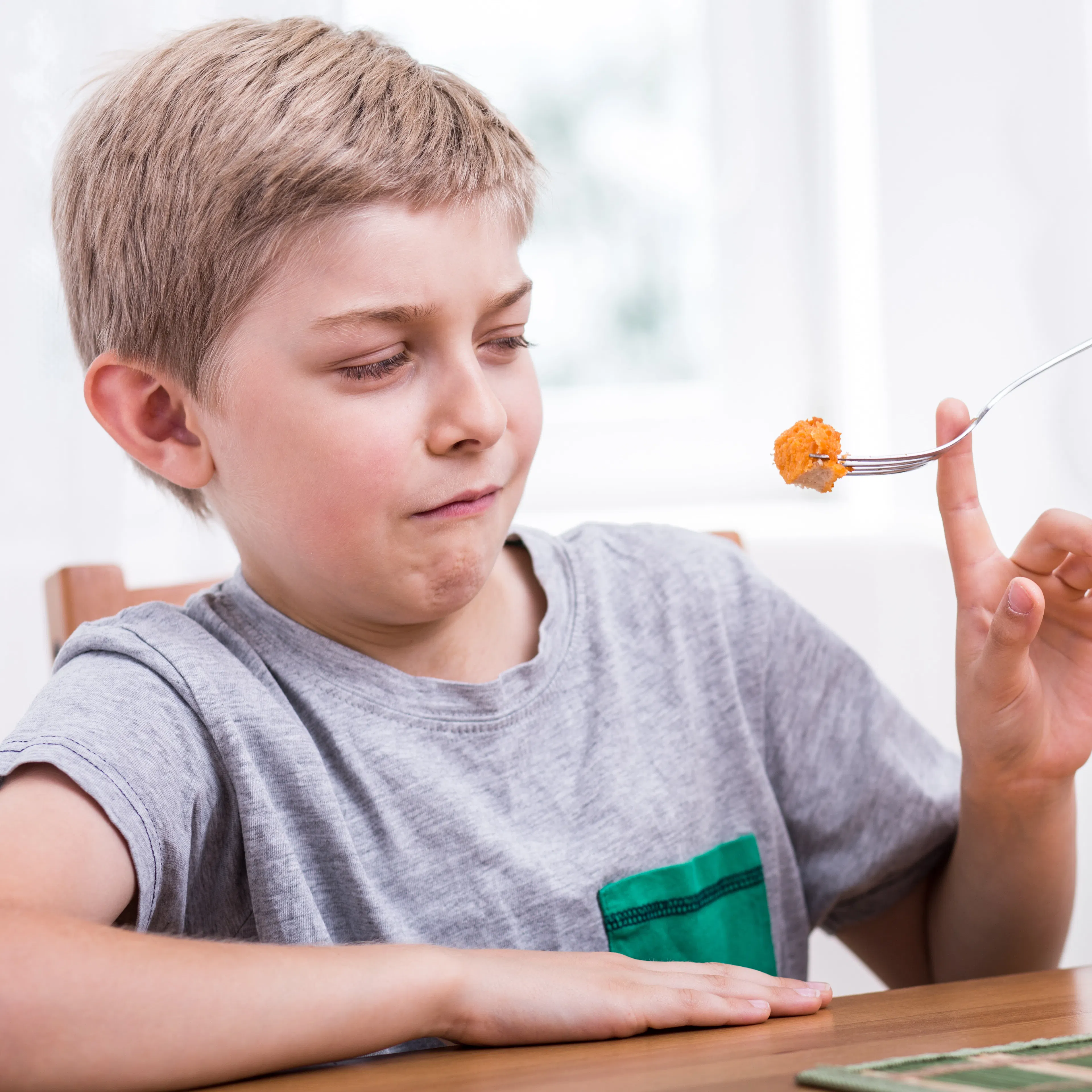 A picky young boy is resisting food he is being fed on a fork.