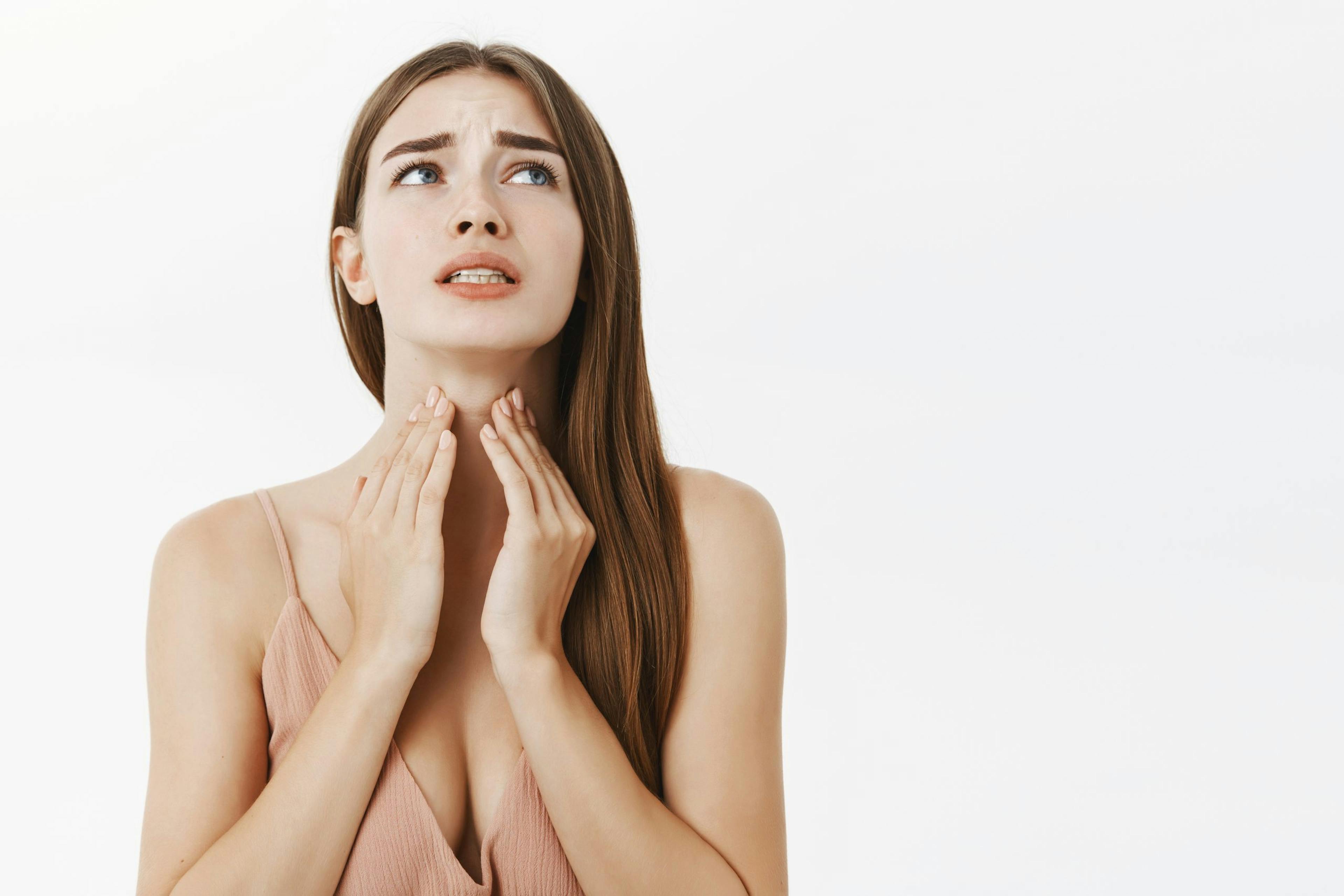 Woman getting ill before important meeting feeling discomfort and suffering from pain in throat touching neck frowning an clenching teeth from terrible feeling posing over gray background