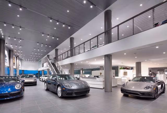Porsche showroom featuring multiple vehicles displayed inside a modern exhibition space with architectural steel elements.
