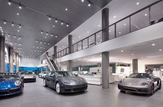 Porsche showroom featuring multiple vehicles displayed inside a modern exhibition space with architectural steel elements.