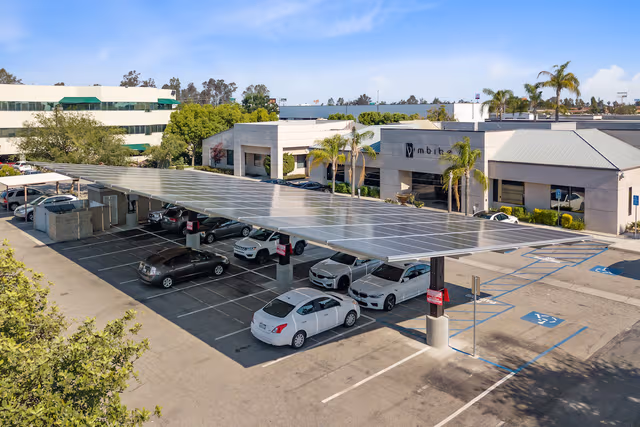 Large parking canopy with several cars underneath and solar panels on the roof, supported by galvanized steel structures protected by Coatinc US.