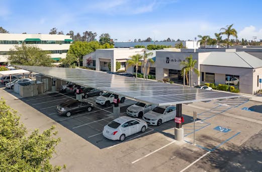 Large parking canopy with several cars underneath and solar panels on the roof, supported by galvanized steel structures protected by Coatinc US.