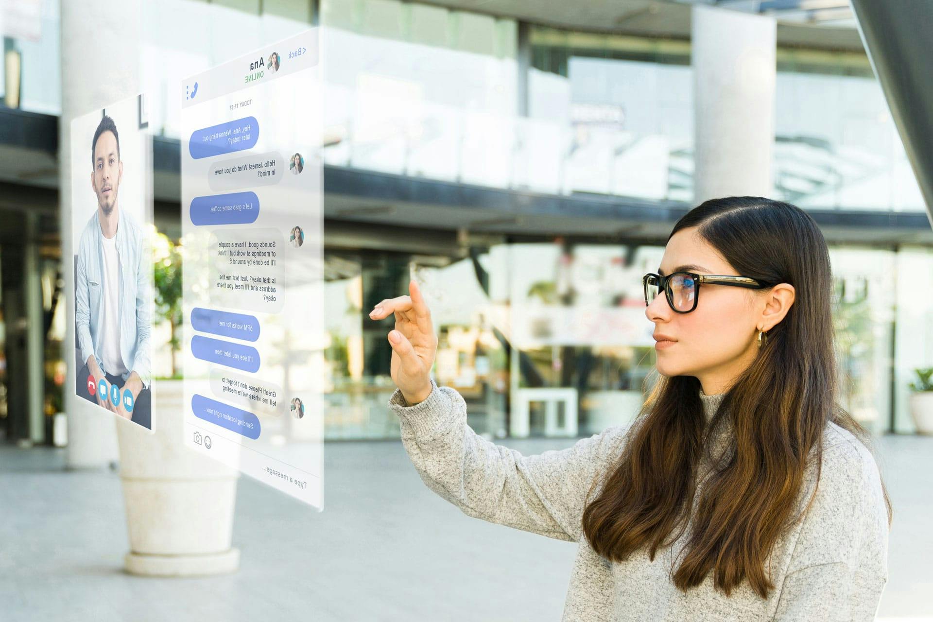 A woman wearing AR glasses interacts with a holographic interface outdoors in a modern setting.