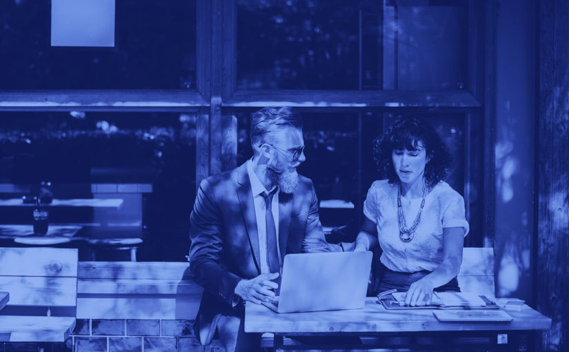 Two professionals discuss work over a laptop at an outdoor café.