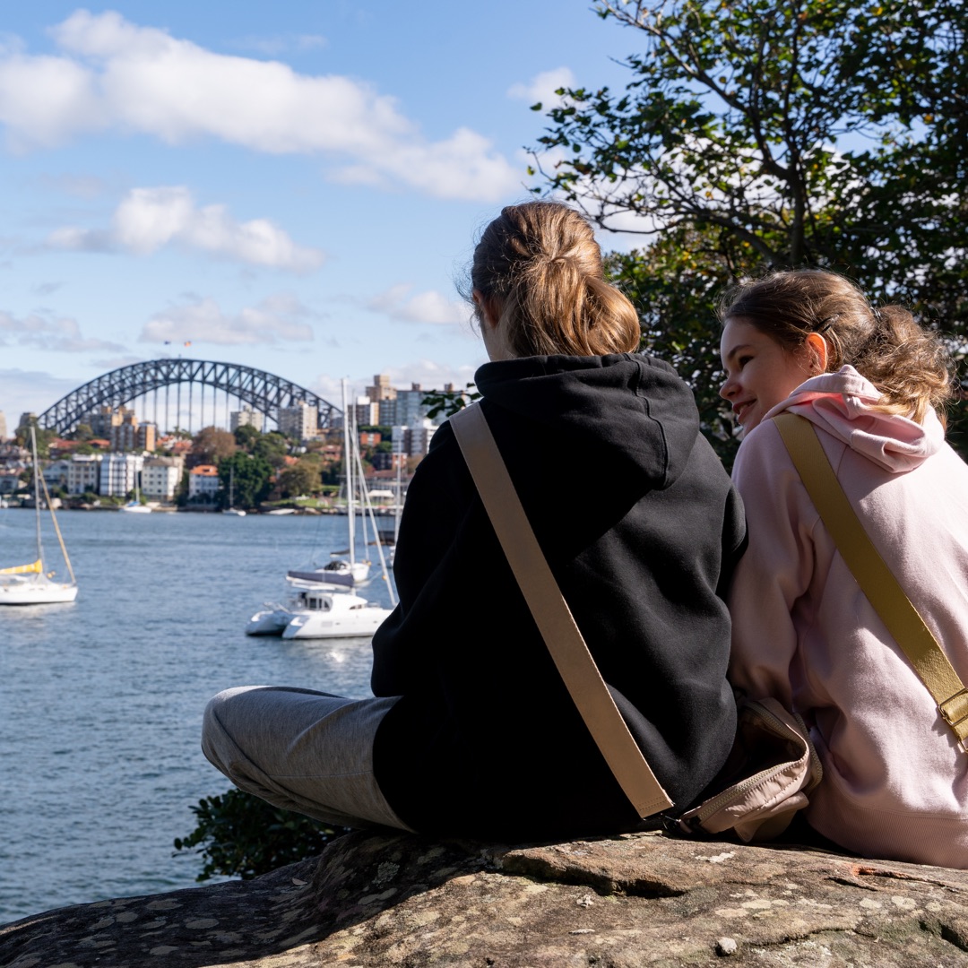 Two students sit under the Sydney Harbour Bridge.