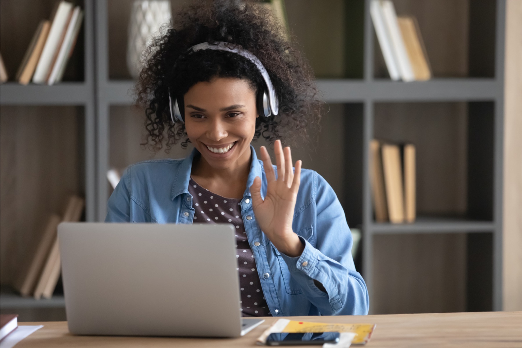 Person with headphones waving at a laptop screen.