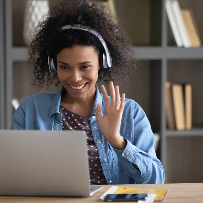 Person with headphones waving at a laptop screen.