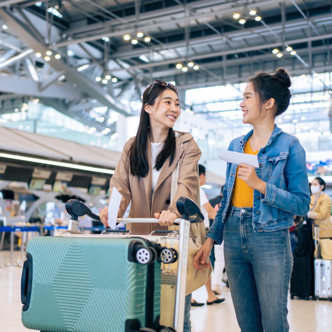 Two women smiling at an airport with luggage.