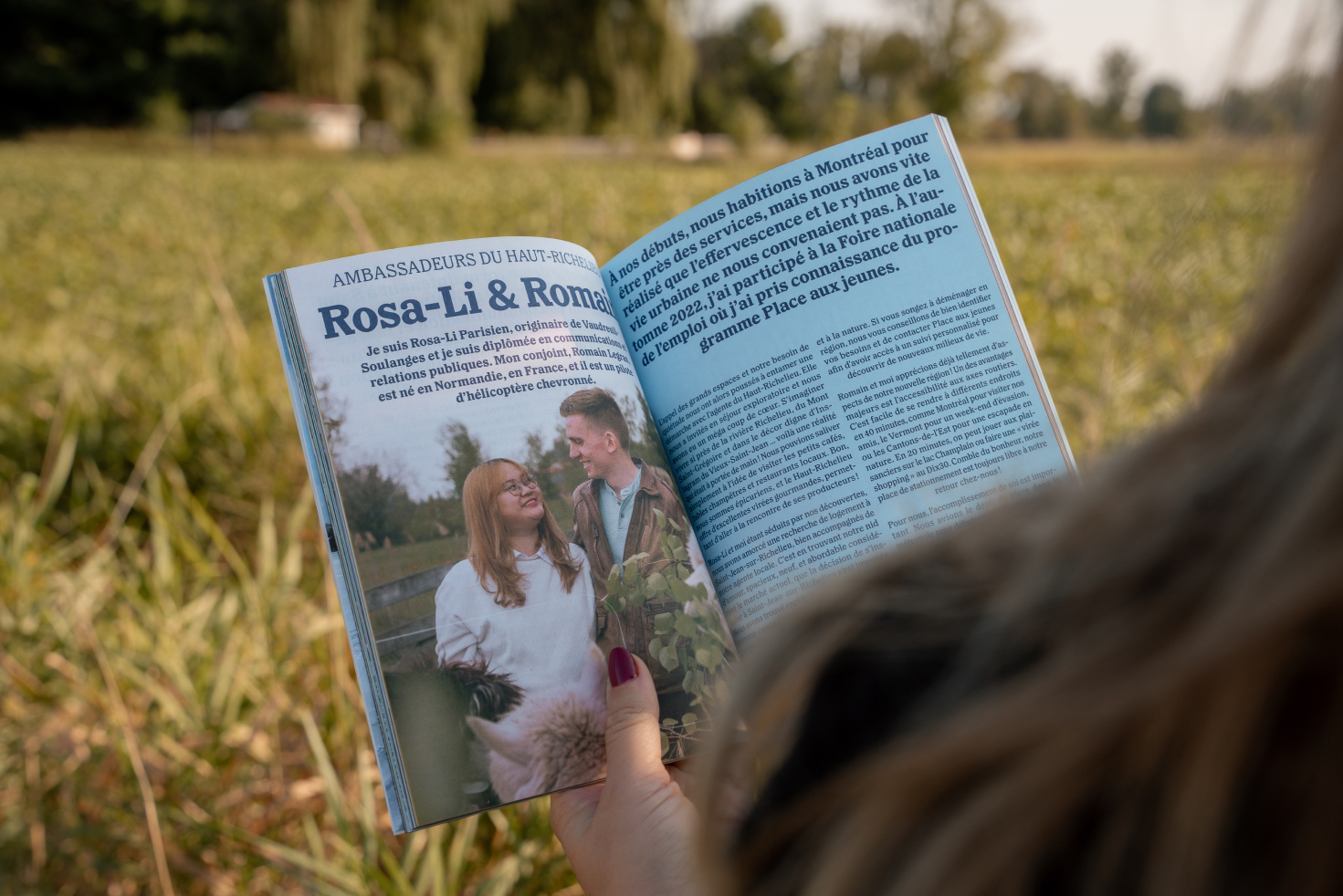 Personne lisant un magazine en plein air, avec un article intitulé ‘Rosa-Li & Romain, Ambassadeurs du Haut-Richelieu’, illustré par une photo d’un couple souriant dans un paysage rural.