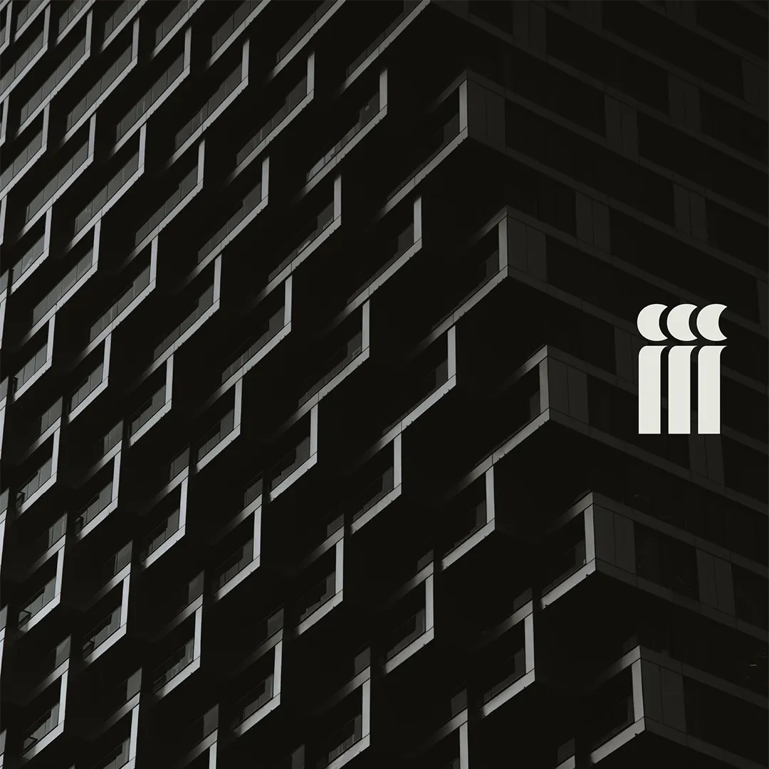 Façade sombre d'un immeuble moderne avec des motifs géométriques en relief, logo minimaliste blanc composé de trois formes verticales avec croissants en haut à droite.