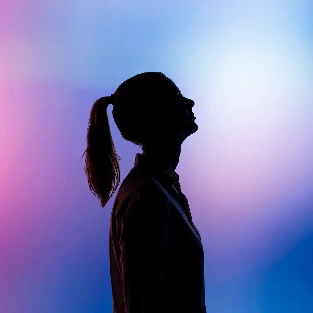 Silhouette d'une femme de profil, les cheveux attachés en queue de cheval, sur un fond dégradé de couleurs violettes, roses et bleues.