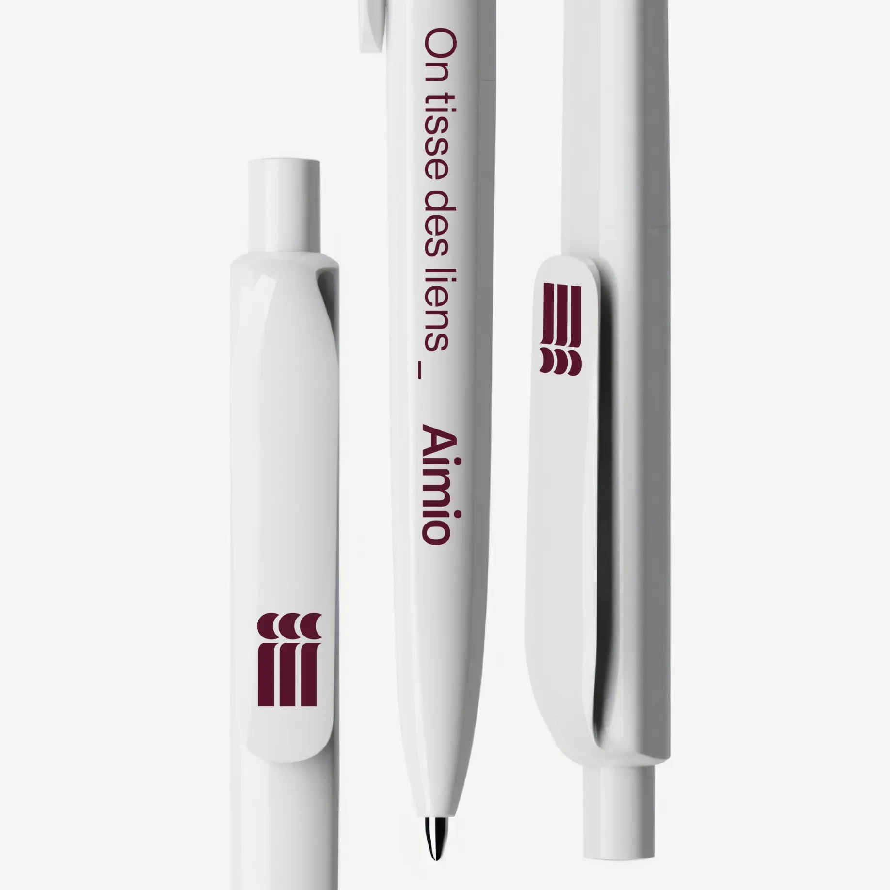 Stylos blancs personnalisés avec le texte « On tisse des liens - Aimio » et un logo minimaliste bordeaux composé de trois formes verticales avec croissants.