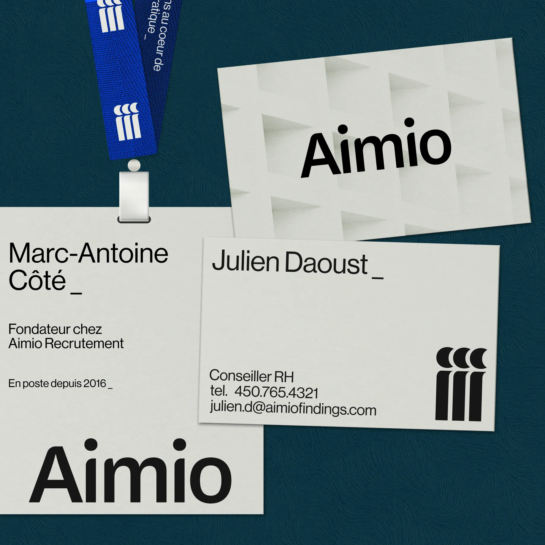 Ensemble d'éléments de branding Aimio sur un fond texturé bleu : badge avec lanière bleue portant le logo Aimio, cartes de visite pour Marc-Antoine Côté et Julien Daoust, avec informations de contact et design minimaliste.