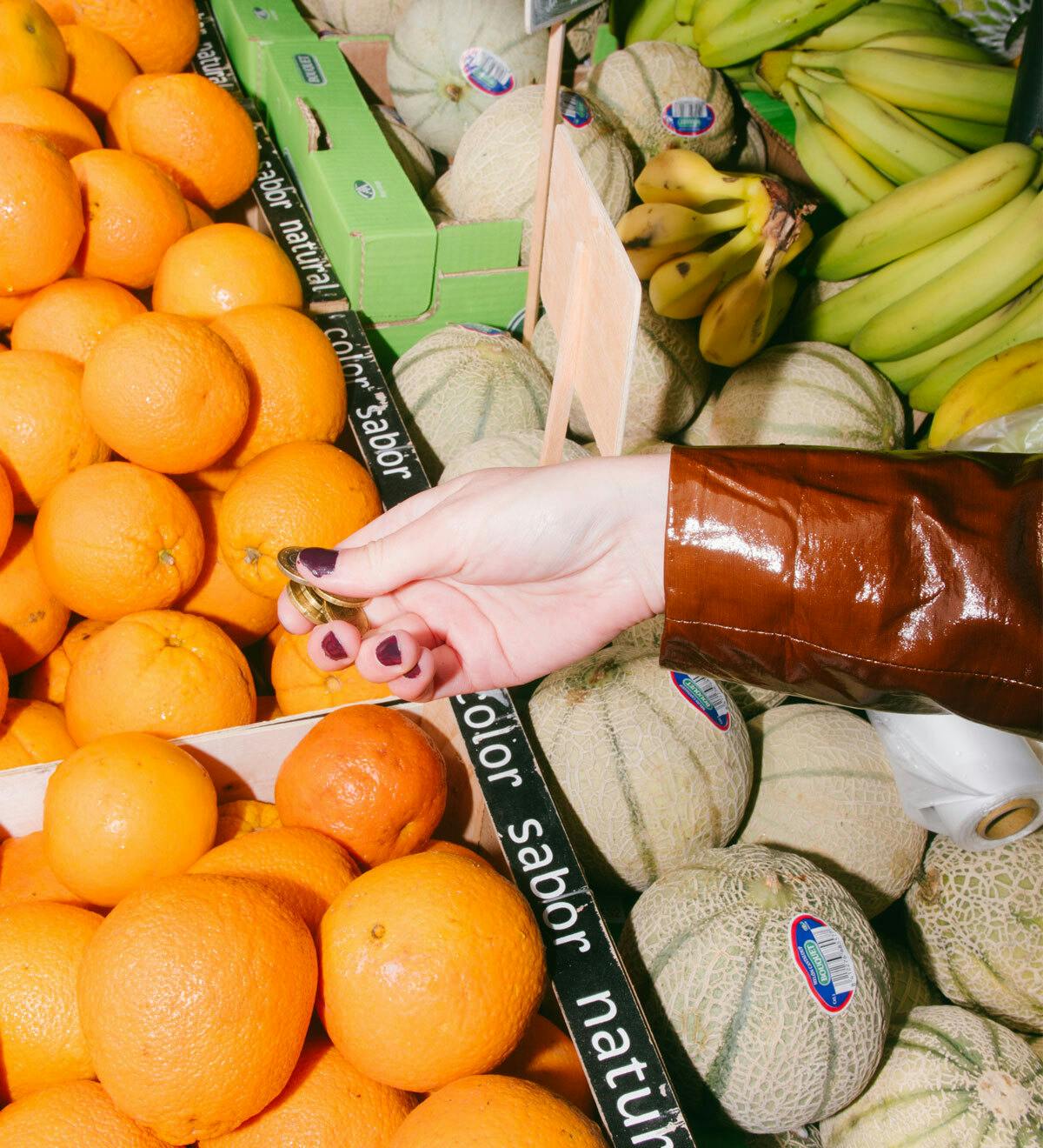 Una mano sujetando monedas para pagar en un puesto de fruta.