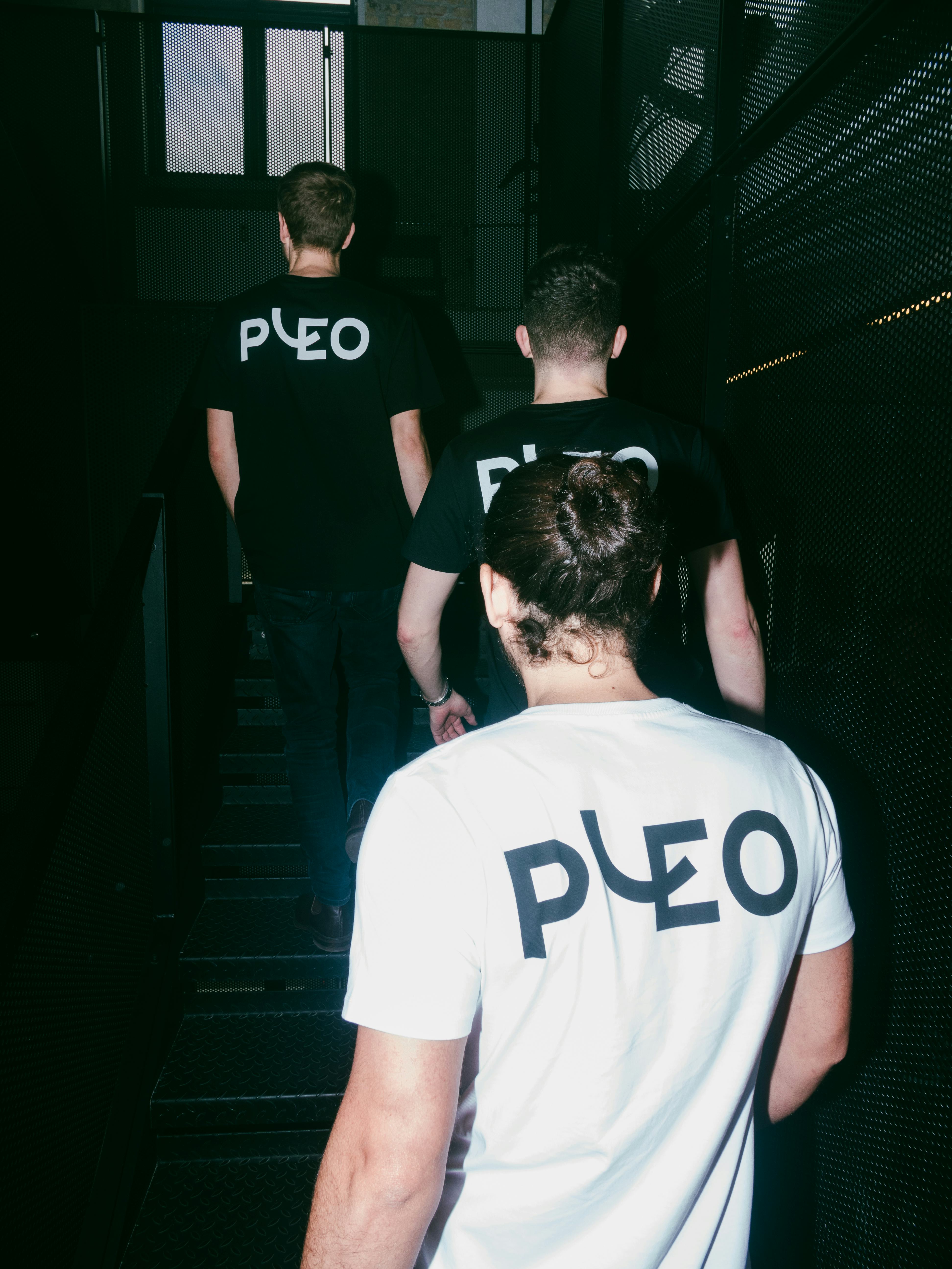 A photograph of three Pleo employees walking up the stairs wearing T shirts with the Pleo logo on the back
