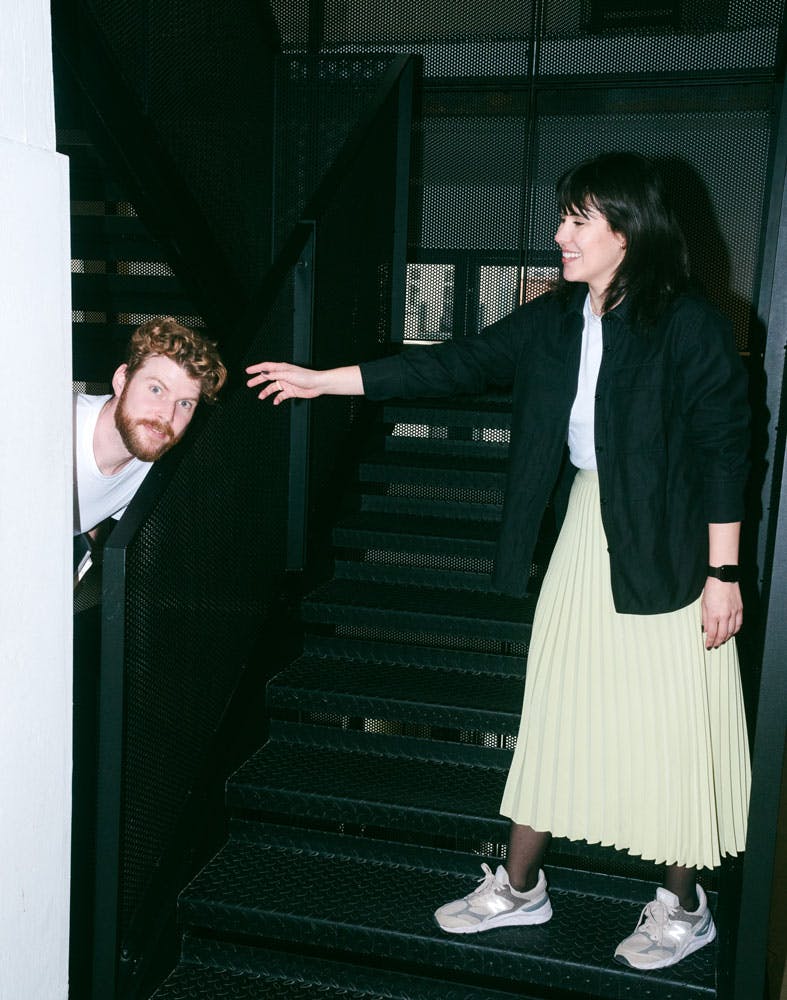 A photo of two Pleo employees; one peaking their head in from the left, the other standing with their hand reached out to them