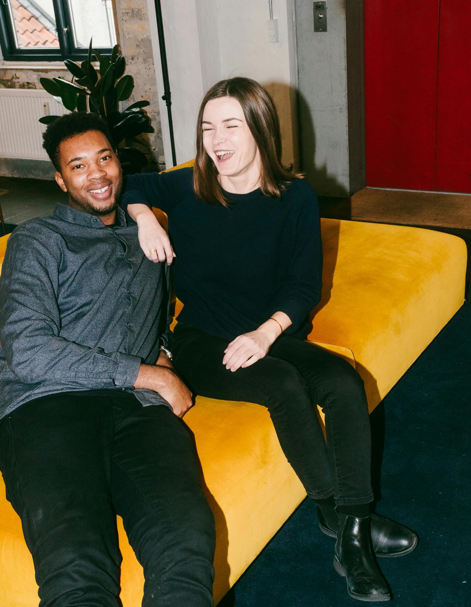 A photograph of two Pleo employees sitting on a yellow sofa in the Copenhagen office