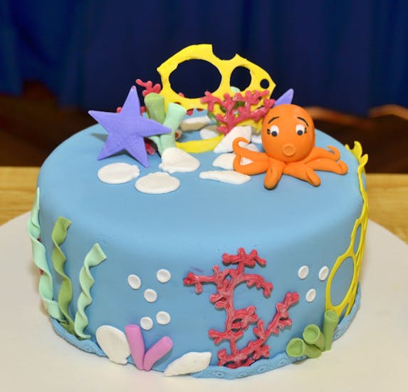a cake that has been decorated to be ocean themed, there is kelp, red coral and a clam on the side with an orange octopus, a purple sea star on the top. 