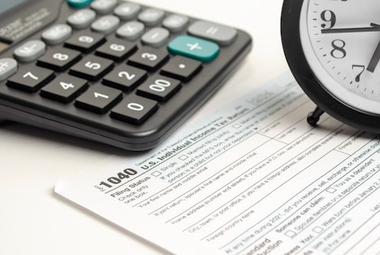 Calculator, tax form, and clock sit on a desk