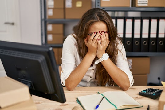 A stressed small business owner hangs her head in frustration over her business taxes.