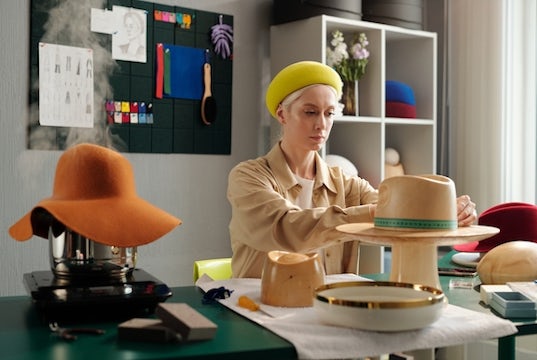 a business owner works to create new hats with her other creations on display