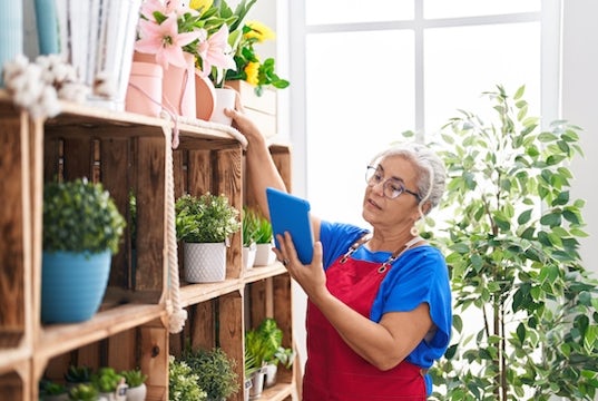 Small business owner checks her inventory by comparing plants on the shelf to the list on her tablet