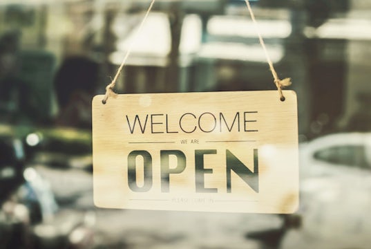 A wooden sign that reads "Welcome, we are open," hangs in a window