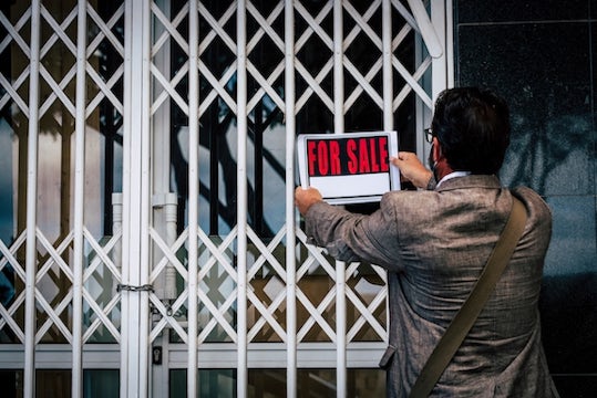 Business owner puts a for sale sign on his closed up shop